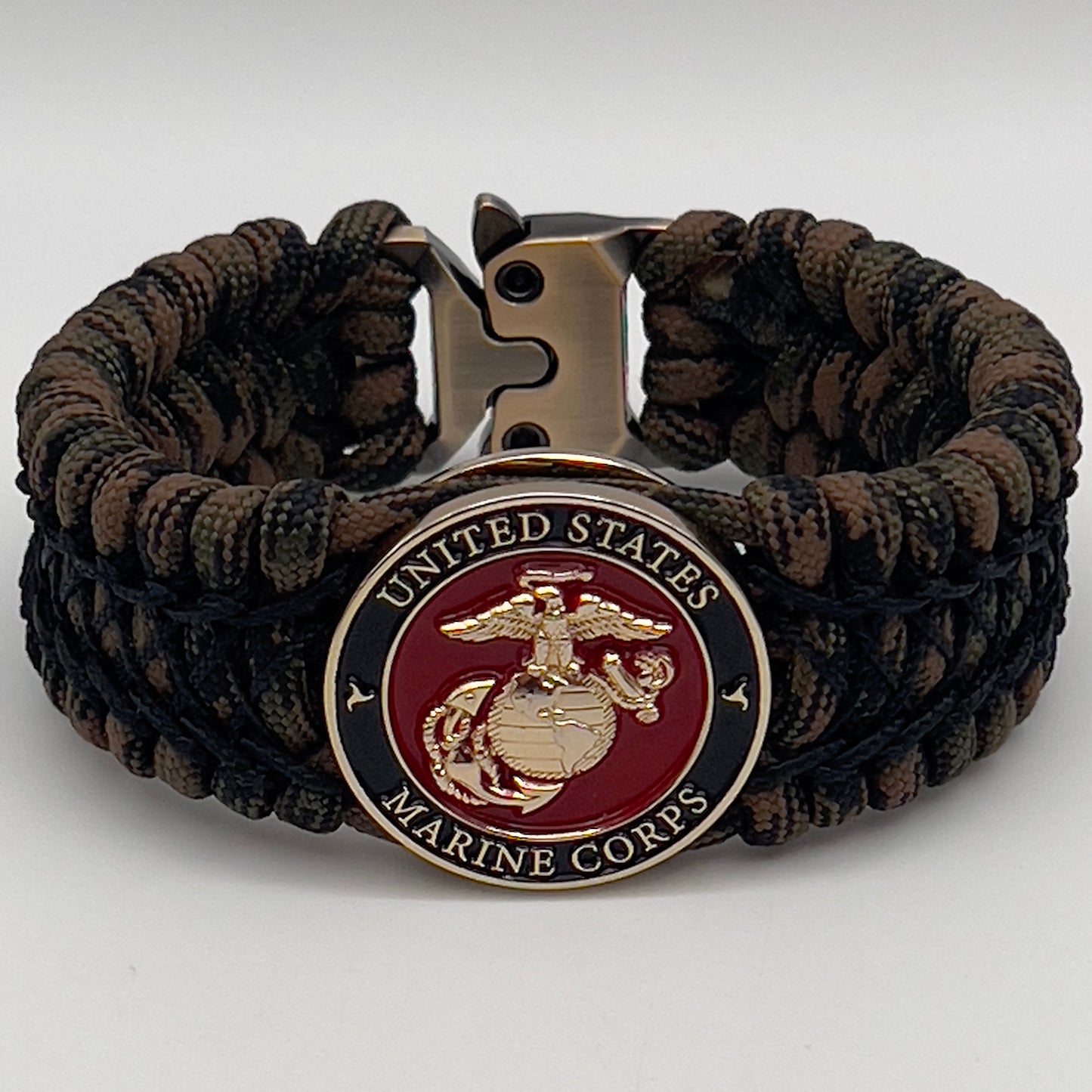 Thick, wide, rigid and comfortable braided United States Marine Corps bracelet featuring a 24K gold plated USMC Eagle Globe and Anchor medallion, a gold Cobra style tactical buckle and woven with Woodland Camo 550 paracord and black nano and micro cord.