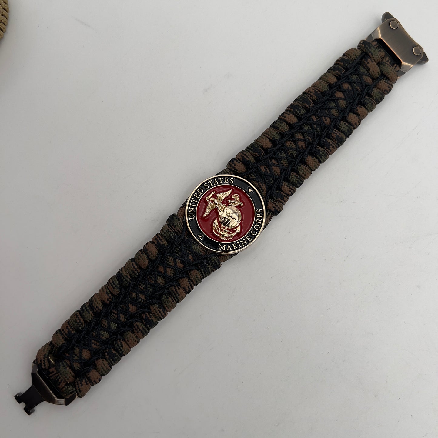 Thick, wide, rigid and comfortable braided United States Marine Corps bracelet featuring a 24K gold plated USMC Eagle Globe and Anchor medallion, a gold Cobra style tactical buckle and woven with Woodland Camo 550 paracord and black nano and micro cord.