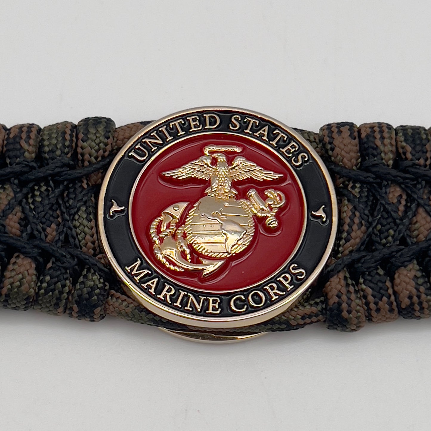 Thick, wide, rigid and comfortable braided United States Marine Corps bracelet featuring a 24K gold plated USMC Eagle Globe and Anchor medallion, a gold Cobra style tactical buckle and woven with Woodland Camo 550 paracord and black nano and micro cord.