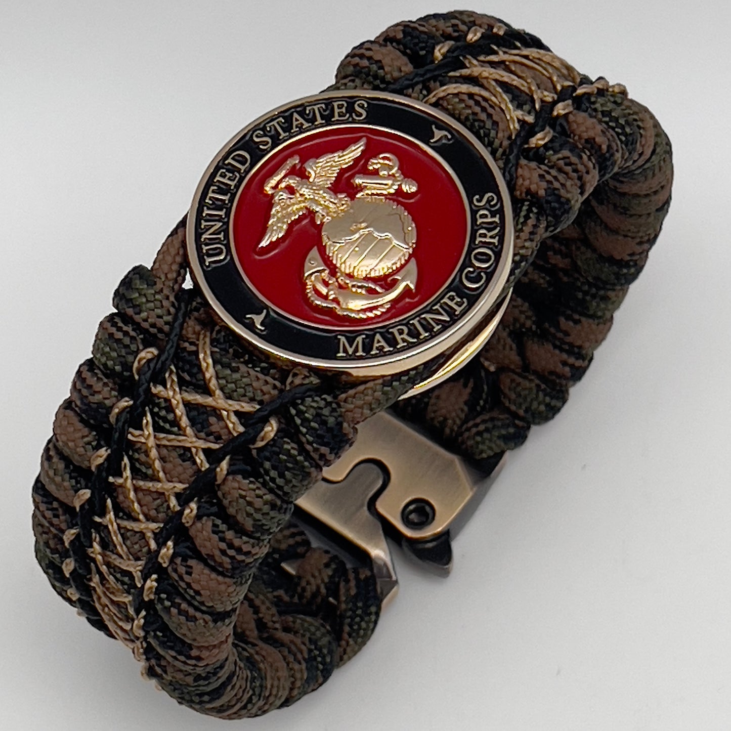 Thick, wide, rigid and comfortable braided United States Marine Corps bracelet featuring a 24K gold plated USMC Eagle Globe and Anchor medallion, a gold Cobra style tactical buckle and woven with Woodland 550 paracord, black micro and tan nano cord.