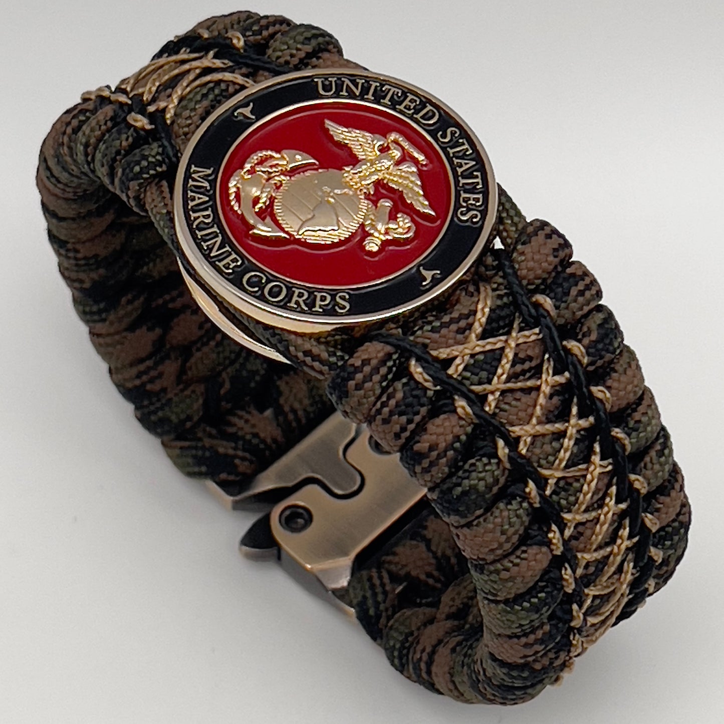 Thick, wide, rigid and comfortable braided United States Marine Corps bracelet featuring a 24K gold plated USMC Eagle Globe and Anchor medallion, a gold Cobra style tactical buckle and woven with Woodland 550 paracord, black micro and tan nano cord.