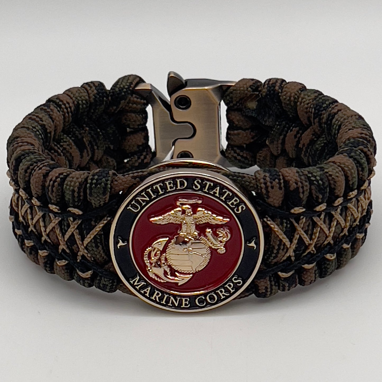 Thick, wide, rigid and comfortable braided United States Marine Corps bracelet featuring a 24K gold plated USMC Eagle Globe and Anchor medallion, a gold Cobra style tactical buckle and woven with Woodland 550 paracord, black micro and tan nano cord.