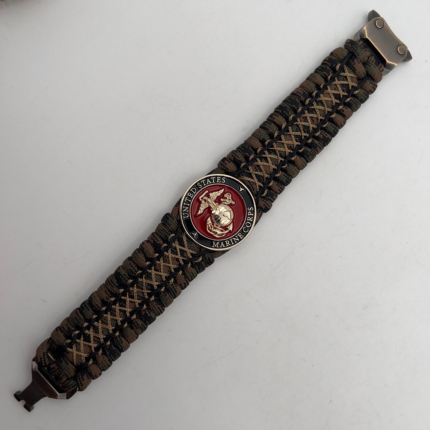 Thick, wide, rigid and comfortable braided United States Marine Corps bracelet featuring a 24K gold plated USMC Eagle Globe and Anchor medallion, a gold Cobra style tactical buckle and woven with Woodland 550 paracord, black micro and tan nano cord.