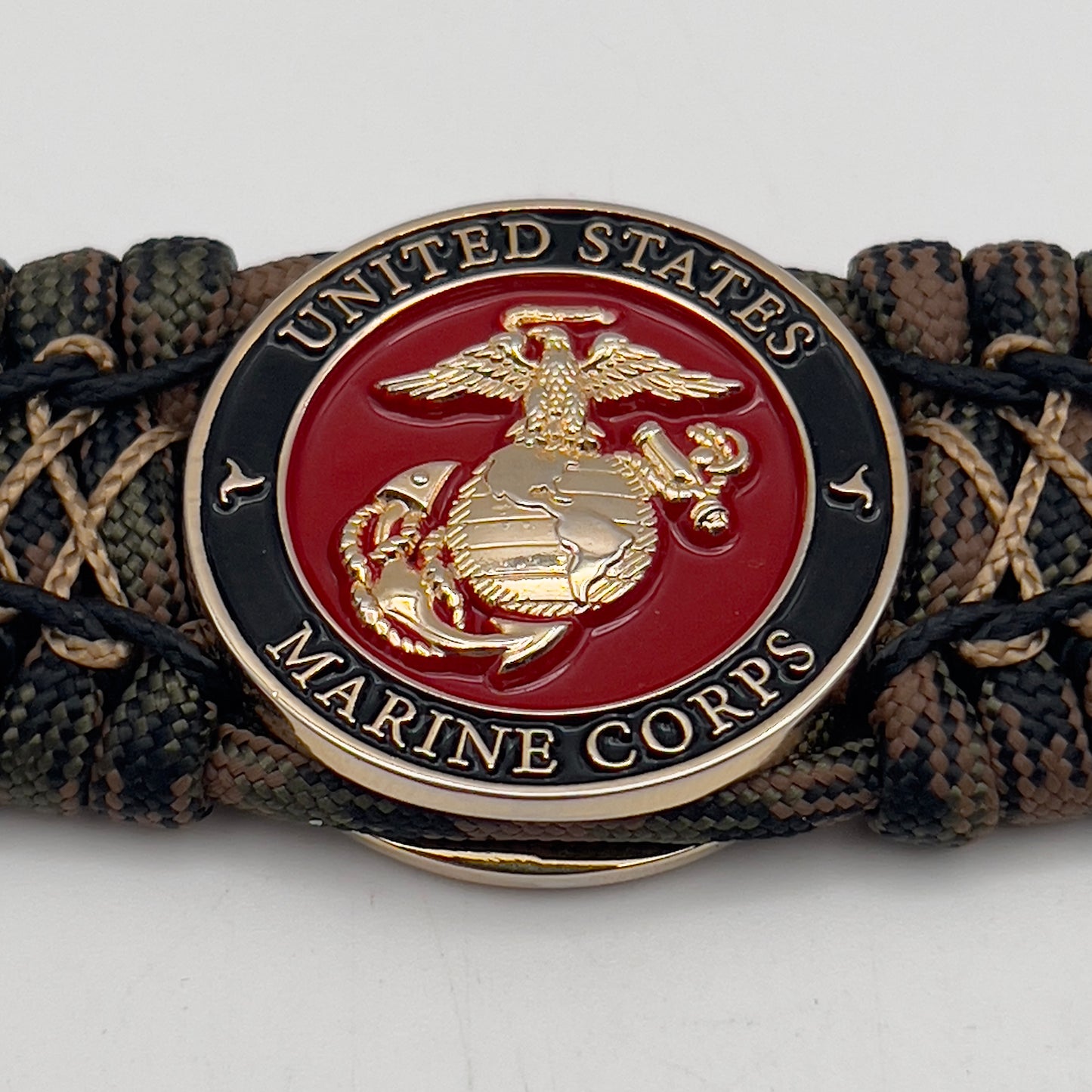 Thick, wide, rigid and comfortable braided United States Marine Corps bracelet featuring a 24K gold plated USMC Eagle Globe and Anchor medallion, a gold Cobra style tactical buckle and woven with Woodland 550 paracord, black micro and tan nano cord.