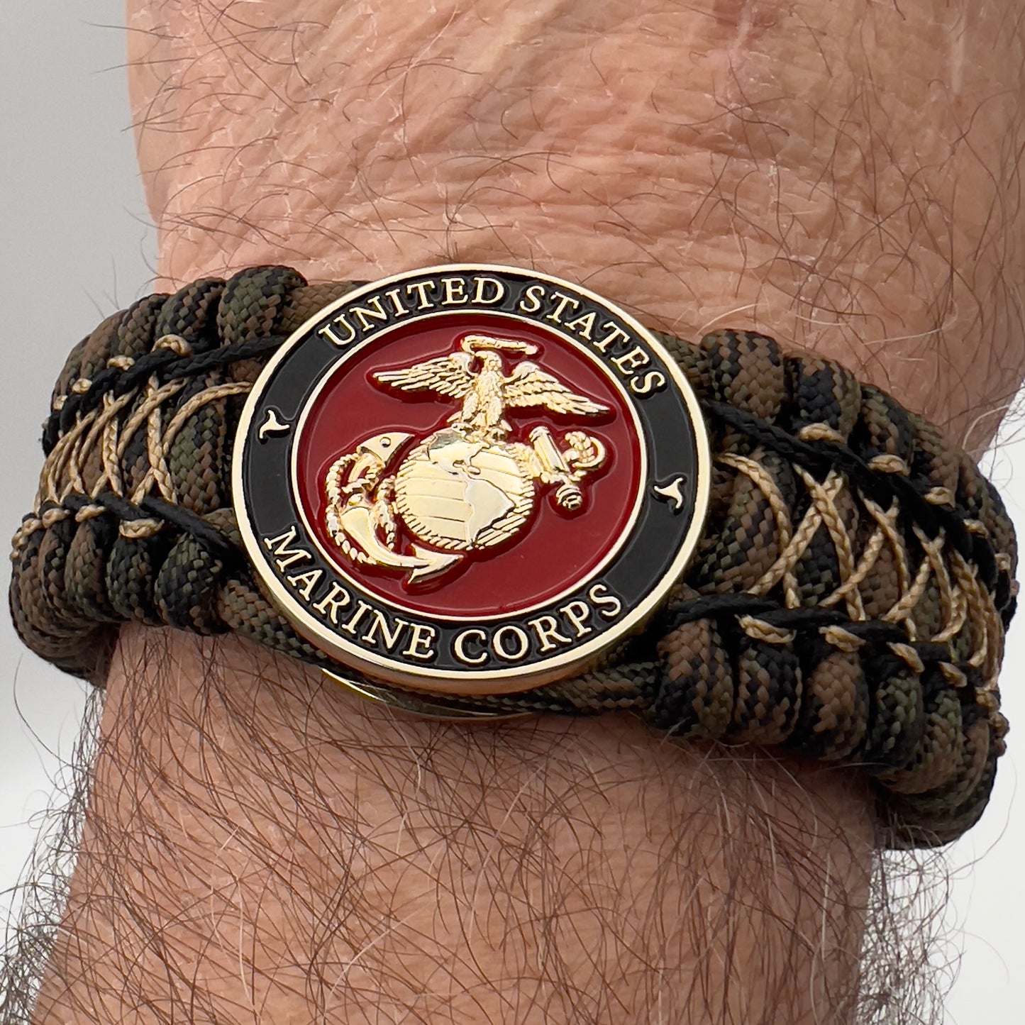 Thick, wide, rigid and comfortable braided United States Marine Corps bracelet featuring a 24K gold plated USMC Eagle Globe and Anchor medallion, a gold Cobra style tactical buckle and woven with Woodland 550 paracord, black micro and tan nano cord.
