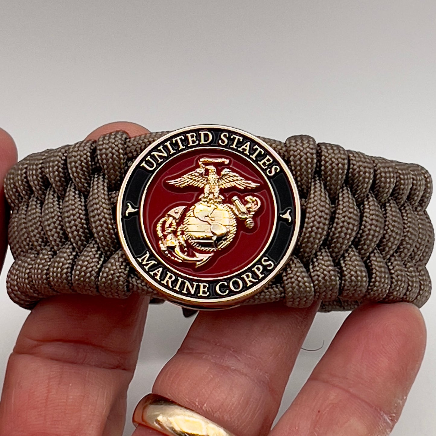 Thick, wide, semi-rigid and comfortable braided United States Marine Corps bracelet featuring a 24K gold plated USMC Eagle Globe and Anchor medallion, a gold Cobra style tactical buckle and woven with tan 550 paracord.
