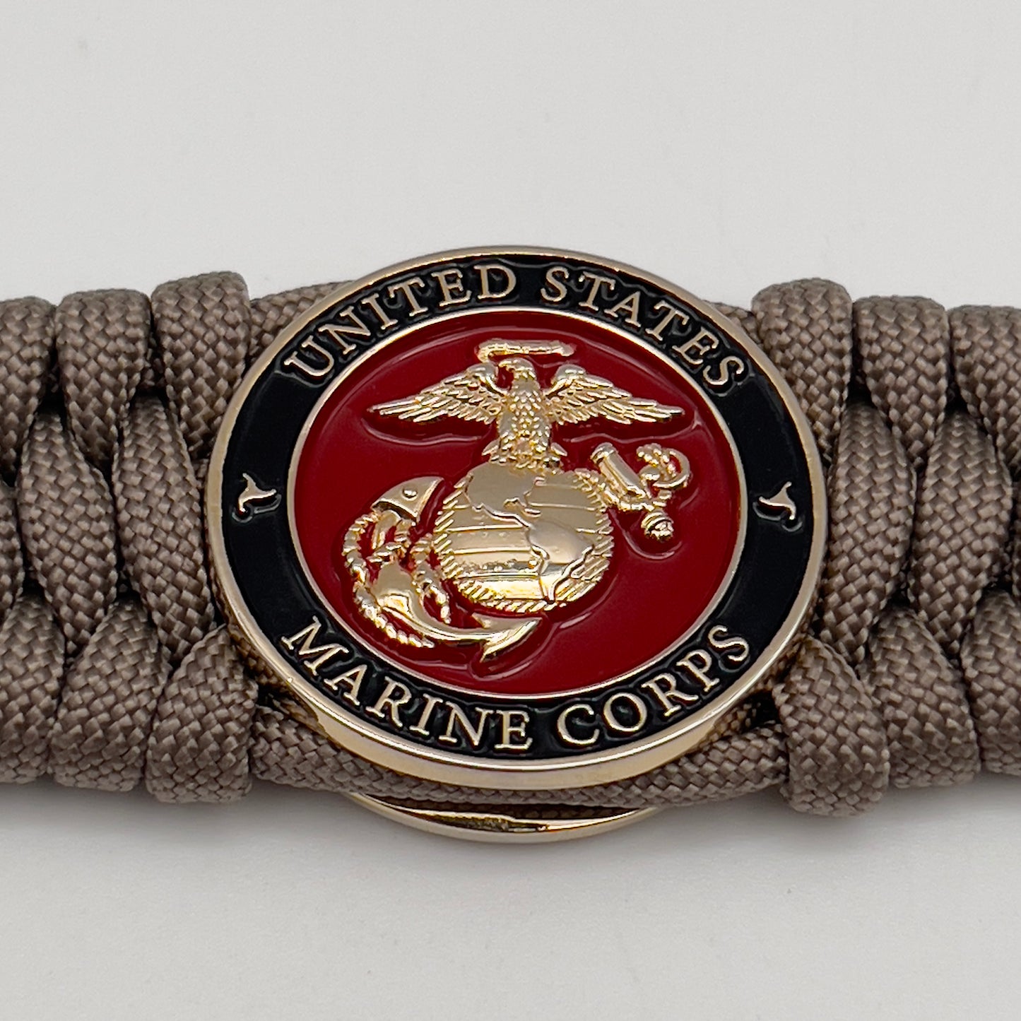 Thick, wide, semi-rigid and comfortable braided United States Marine Corps bracelet featuring a 24K gold plated USMC Eagle Globe and Anchor medallion, a gold Cobra style tactical buckle and woven with tan 550 paracord.