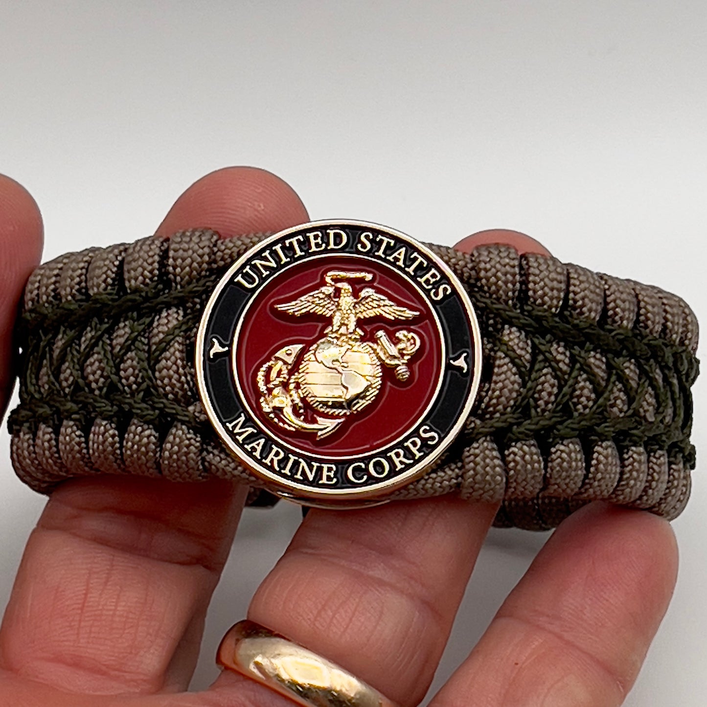 Thick, wide, rigid and comfortable braided United States Marine Corps bracelet featuring a 24K gold plated USMC Eagle Globe and Anchor medallion, a gold Cobra style tactical buckle and woven with tan 550 paracord and olive drab nano and micro cord.