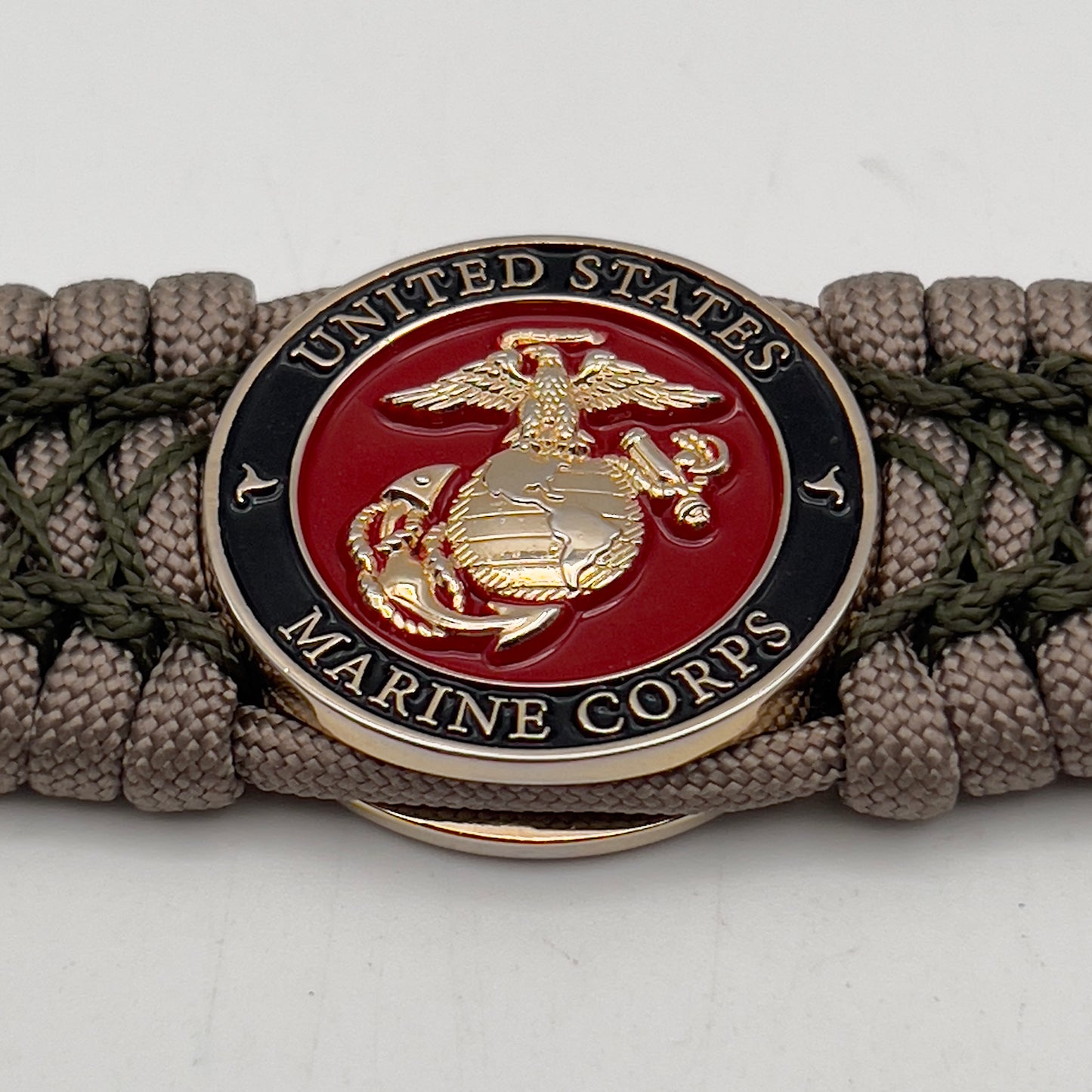 Thick, wide, rigid and comfortable braided United States Marine Corps bracelet featuring a 24K gold plated USMC Eagle Globe and Anchor medallion, a gold Cobra style tactical buckle and woven with tan 550 paracord and olive drab nano and micro cord.