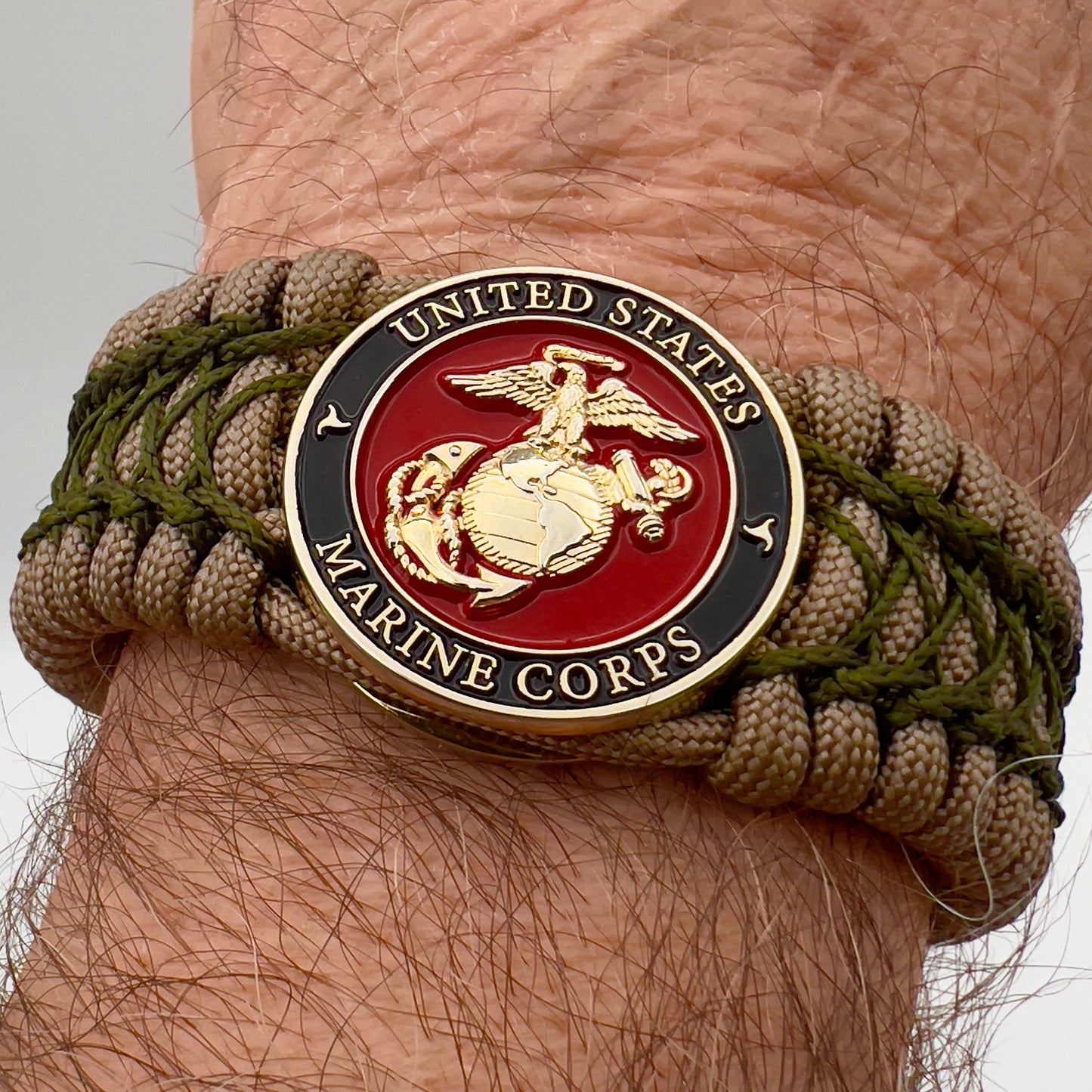 Thick, wide, rigid and comfortable braided United States Marine Corps bracelet featuring a 24K gold plated USMC Eagle Globe and Anchor medallion, a gold Cobra style tactical buckle and woven with tan 550 paracord and olive drab nano and micro cord.