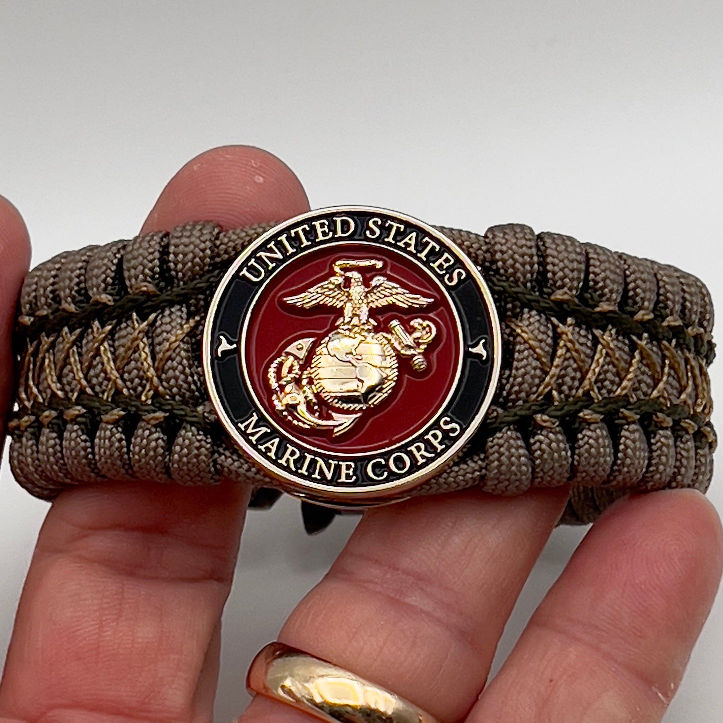 Thick, wide, rigid and comfortable braided United States Marine Corps bracelet featuring a 24K gold plated USMC Eagle Globe and Anchor medallion, a gold Cobra style tactical buckle and woven with tan 550 paracord and olive drab micro and tan nano cord.