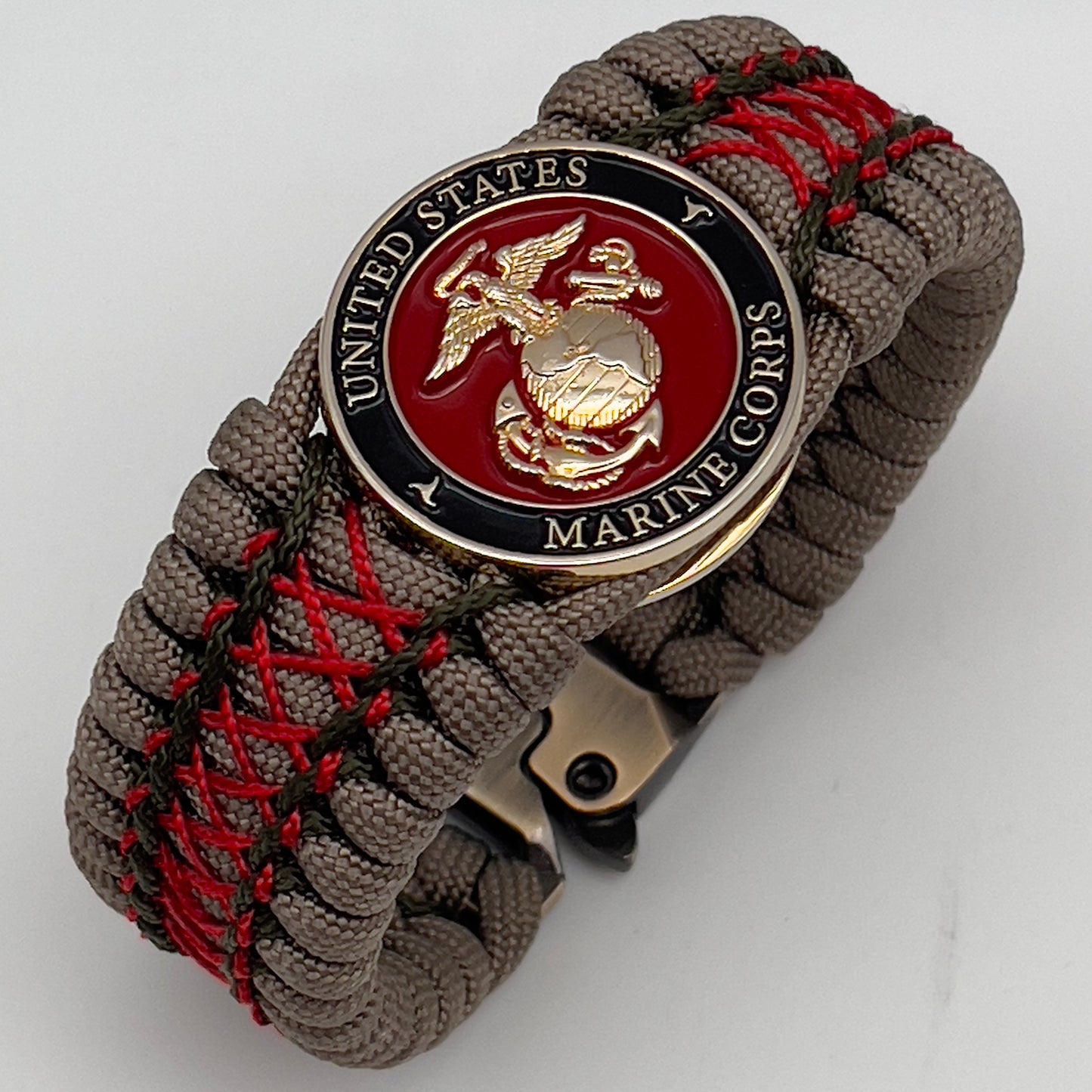 Thick, wide, rigid and comfortable braided United States Marine Corps bracelet featuring a 24K gold plated USMC Eagle Globe and Anchor medallion, a gold Cobra style tactical buckle and woven with tan 550 paracord, olive drab micro and Imperial red nano cord.