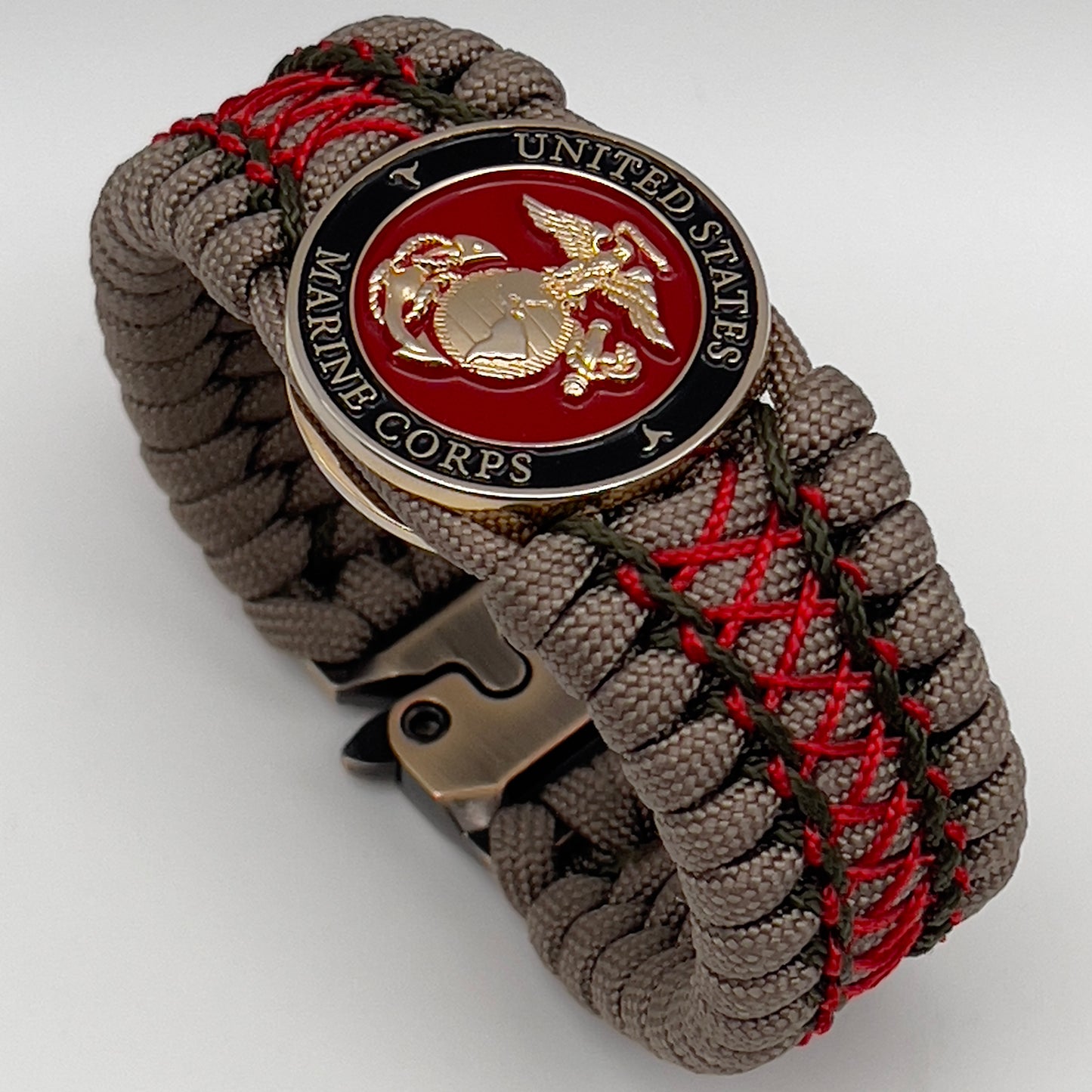 Thick, wide, rigid and comfortable braided United States Marine Corps bracelet featuring a 24K gold plated USMC Eagle Globe and Anchor medallion, a gold Cobra style tactical buckle and woven with tan 550 paracord, olive drab micro and Imperial red nano cord.