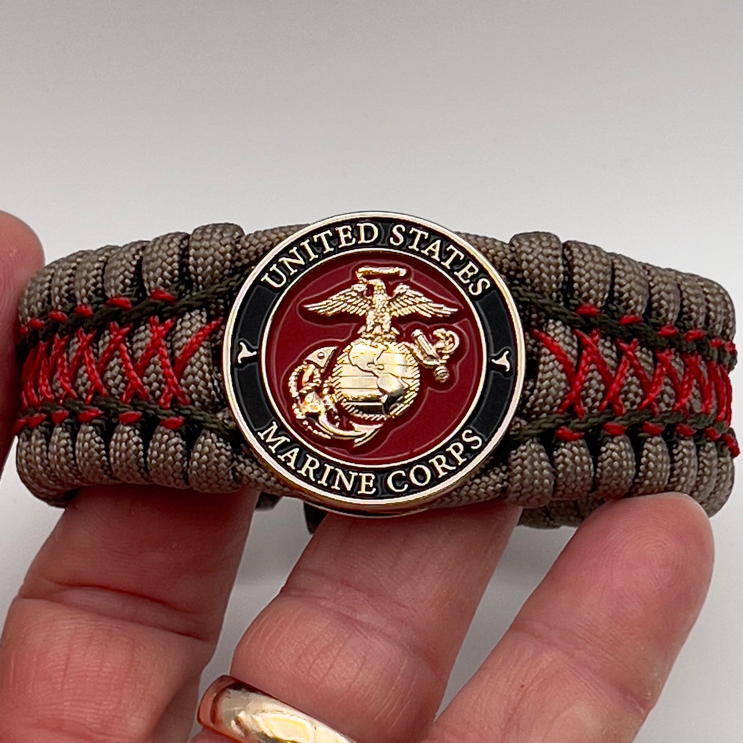 Thick, wide, rigid and comfortable braided United States Marine Corps bracelet featuring a 24K gold plated USMC Eagle Globe and Anchor medallion, a gold Cobra style tactical buckle and woven with tan 550 paracord, olive drab micro and Imperial red nano cord.