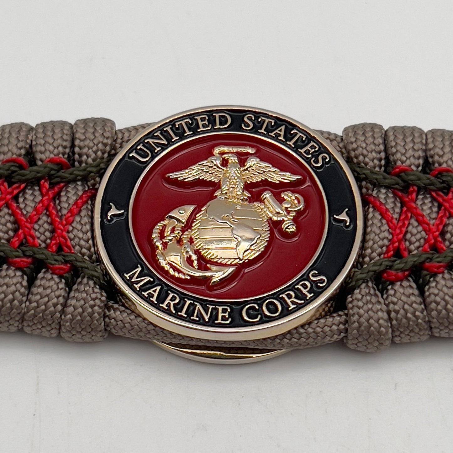 Thick, wide, rigid and comfortable braided United States Marine Corps bracelet featuring a 24K gold plated USMC Eagle Globe and Anchor medallion, a gold Cobra style tactical buckle and woven with tan 550 paracord, olive drab micro and Imperial red nano cord.