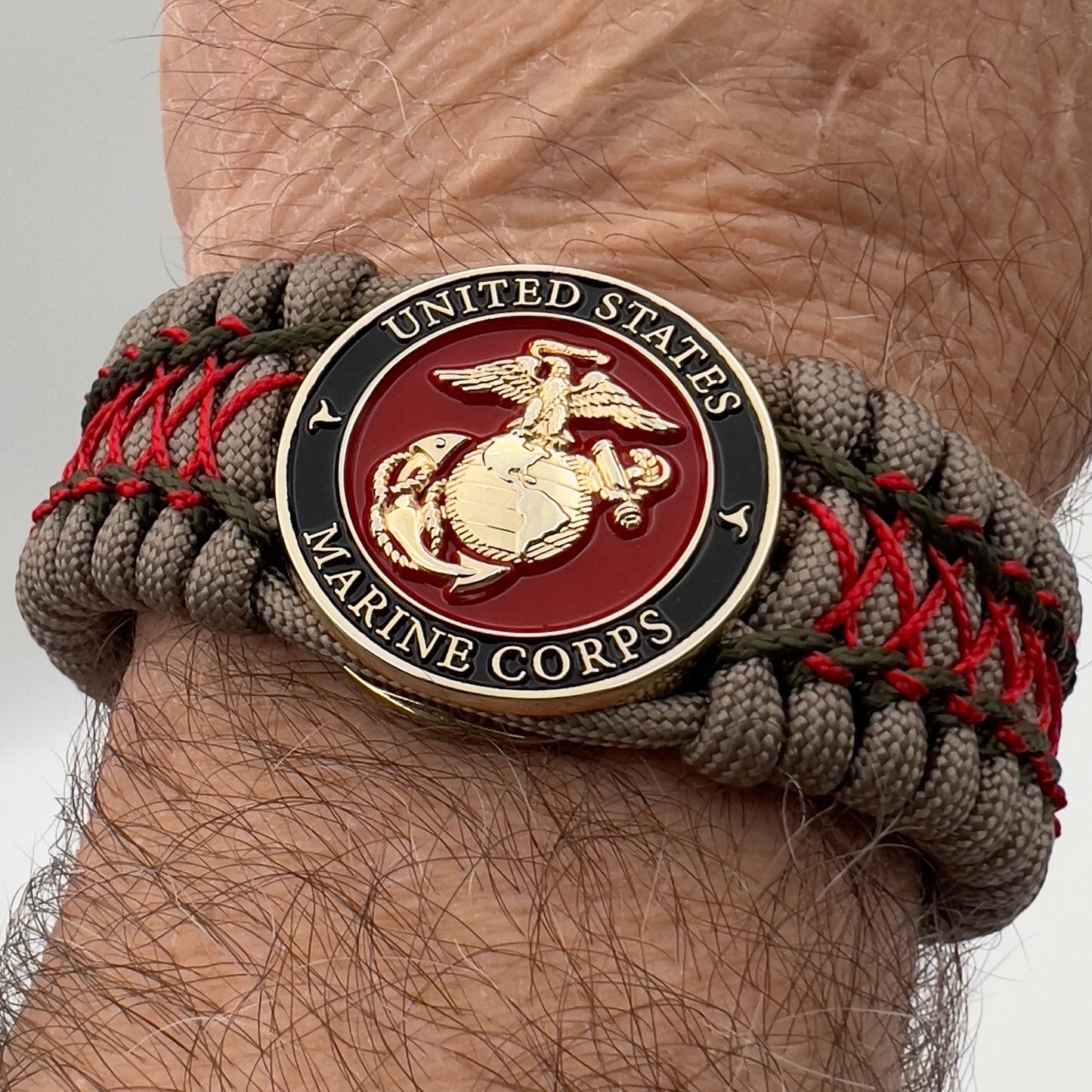 Thick, wide, rigid and comfortable braided United States Marine Corps bracelet featuring a 24K gold plated USMC Eagle Globe and Anchor medallion, a gold Cobra style tactical buckle and woven with tan 550 paracord, olive drab micro and Imperial red nano cord.