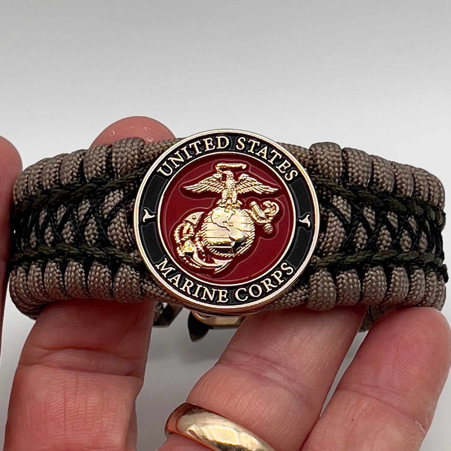 Thick, wide, rigid and comfortable braided United States Marine Corps bracelet featuring a 24K gold plated USMC Eagle Globe and Anchor medallion, a gold Cobra style tactical buckle and woven with tan 550 paracord, olive drab micro and black nano cord.