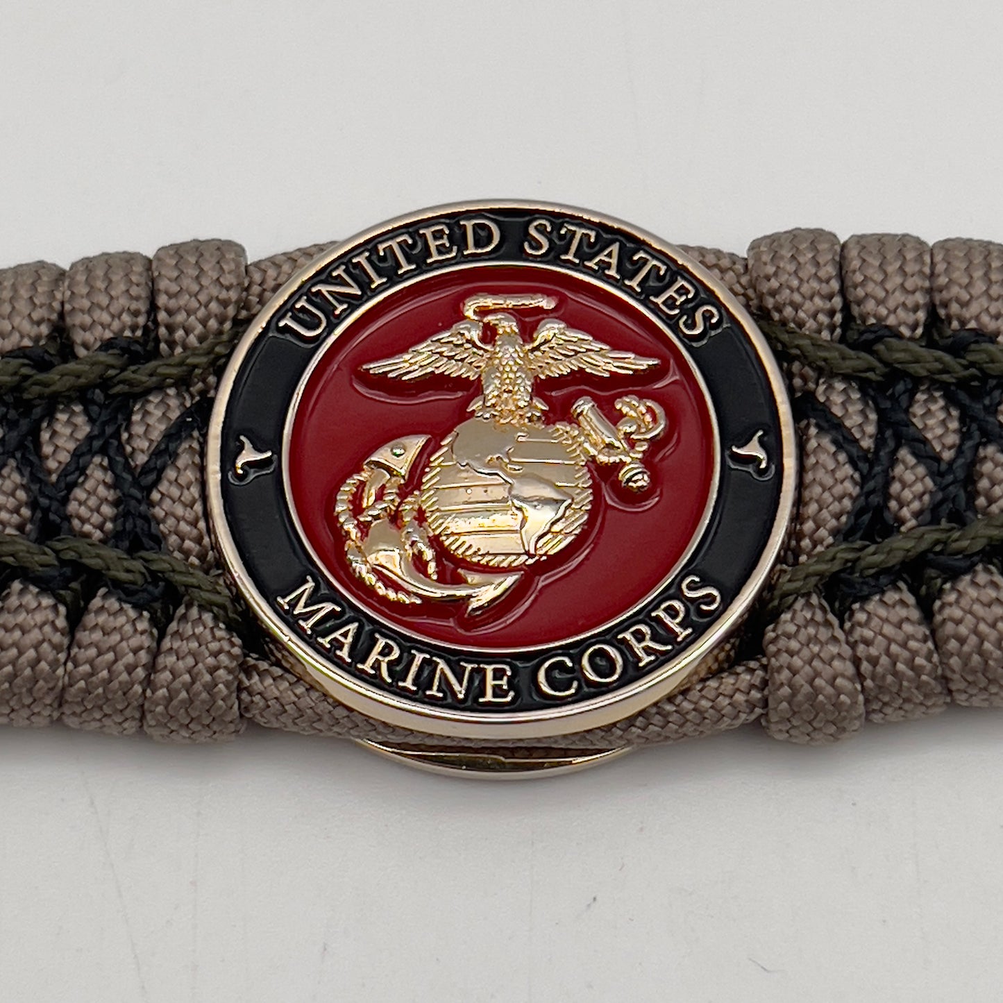 Thick, wide, rigid and comfortable braided United States Marine Corps bracelet featuring a 24K gold plated USMC Eagle Globe and Anchor medallion, a gold Cobra style tactical buckle and woven with tan 550 paracord, olive drab micro and black nano cord.