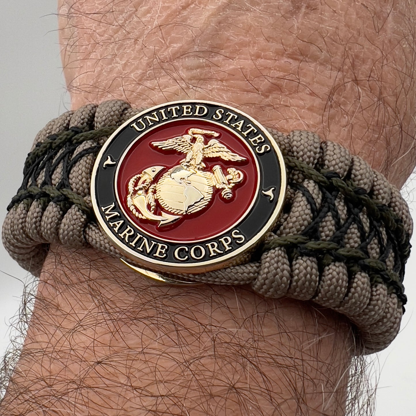 Thick, wide, rigid and comfortable braided United States Marine Corps bracelet featuring a 24K gold plated USMC Eagle Globe and Anchor medallion, a gold Cobra style tactical buckle and woven with tan 550 paracord, olive drab micro and black nano cord.
