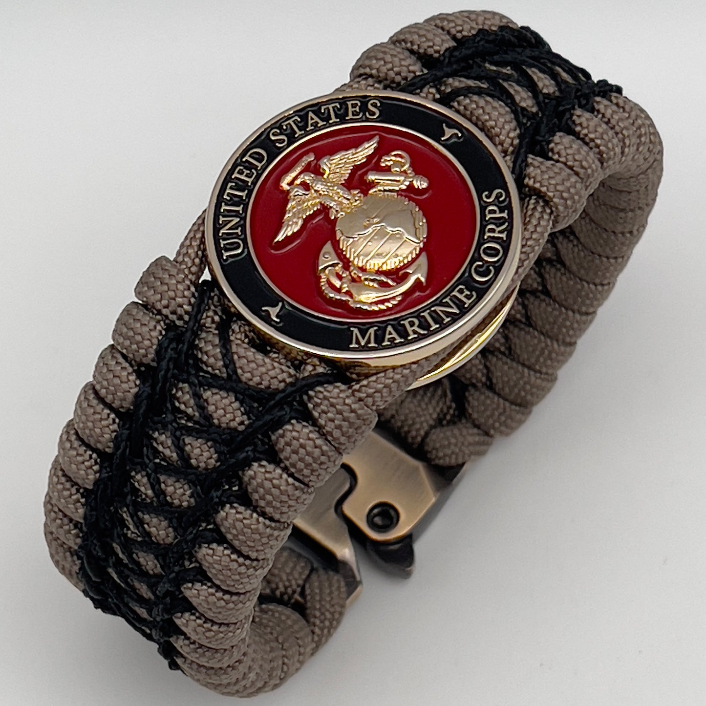 Thick, wide, rigid and comfortable braided United States Marine Corps bracelet featuring a 24K gold plated USMC Eagle Globe and Anchor medallion, a gold Cobra style tactical buckle and woven with tan 550 paracord and black nano and micro cord.
