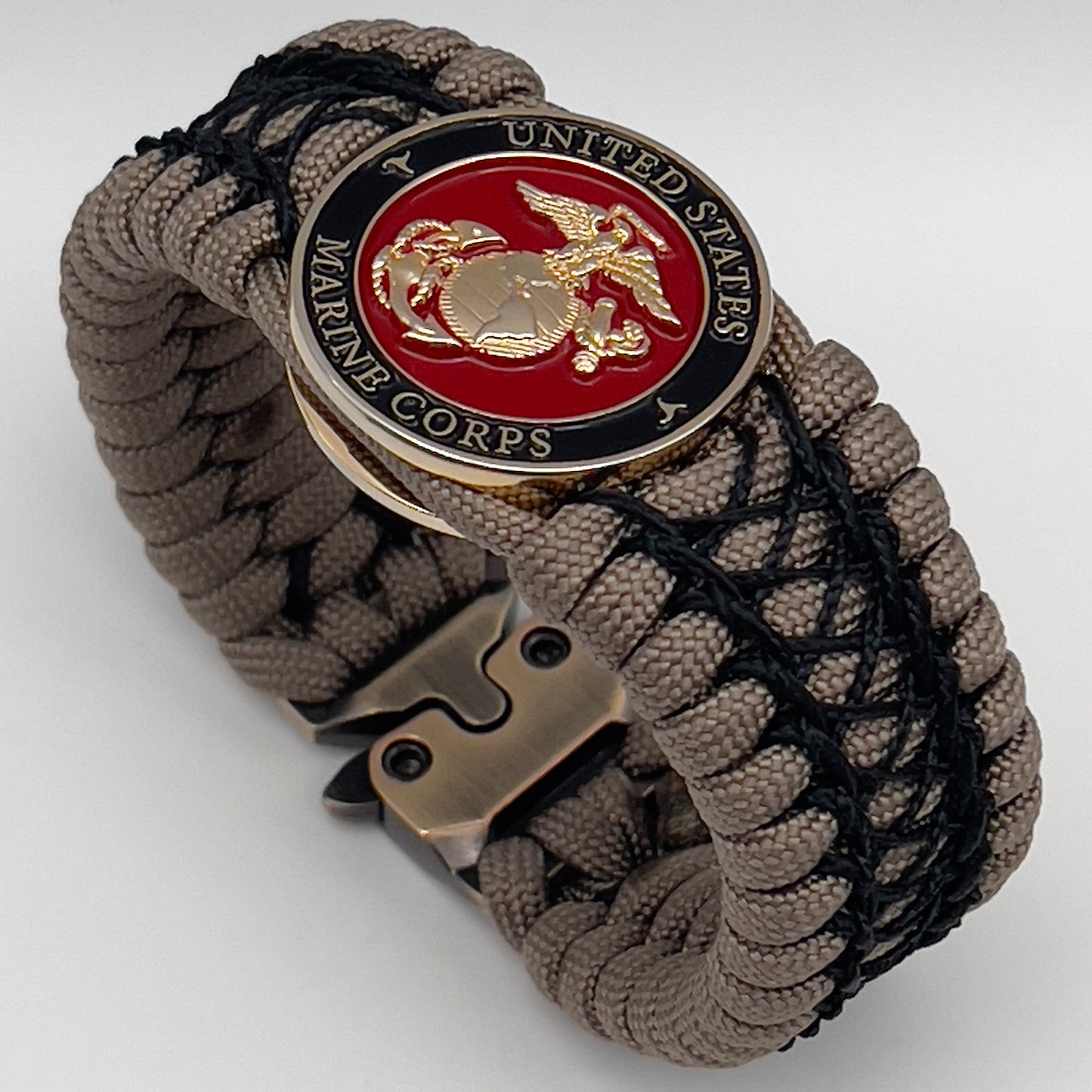 Thick, wide, rigid and comfortable braided United States Marine Corps bracelet featuring a 24K gold plated USMC Eagle Globe and Anchor medallion, a gold Cobra style tactical buckle and woven with tan 550 paracord and black nano and micro cord.