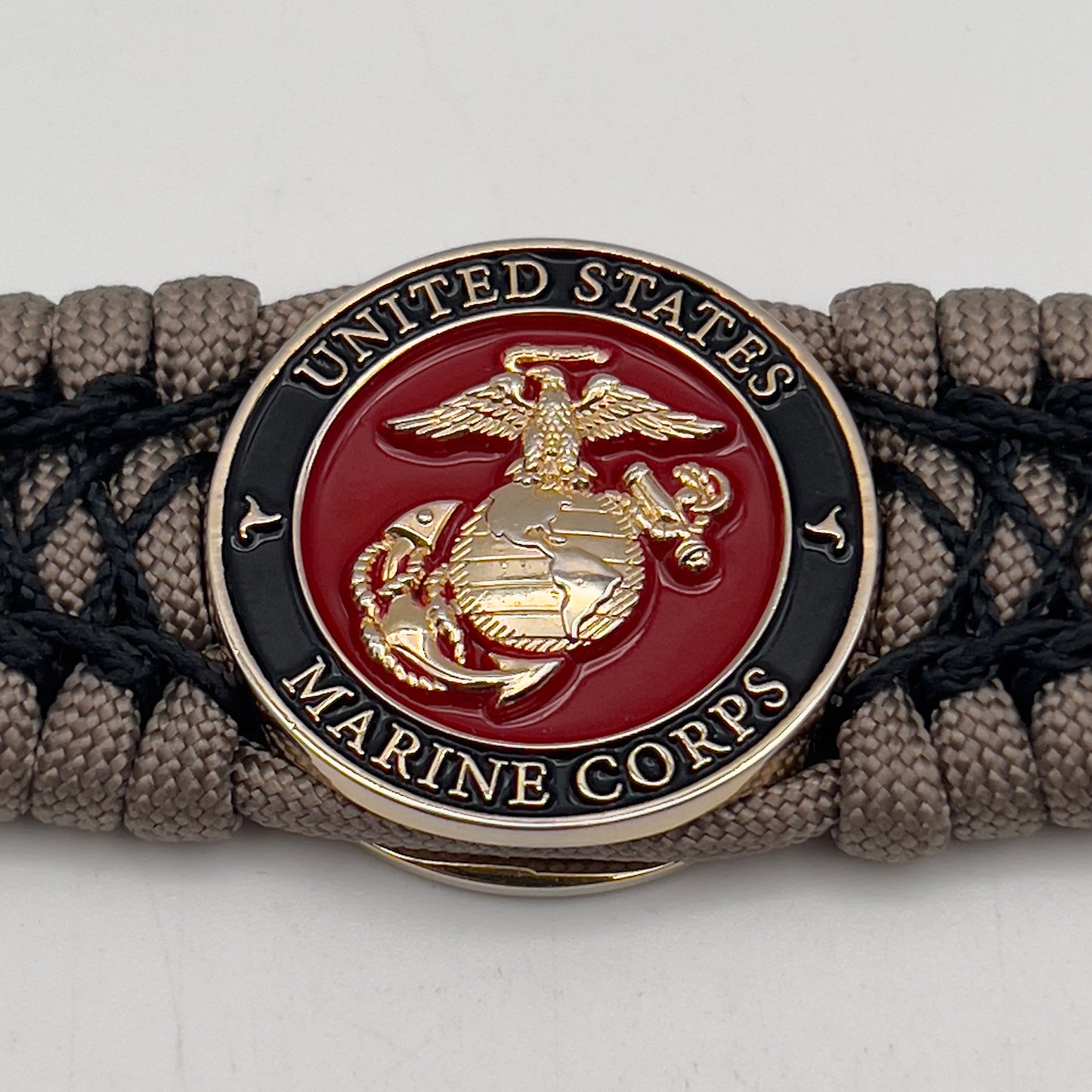 Thick, wide, rigid and comfortable braided United States Marine Corps bracelet featuring a 24K gold plated USMC Eagle Globe and Anchor medallion, a gold Cobra style tactical buckle and woven with tan 550 paracord and black nano and micro cord.
