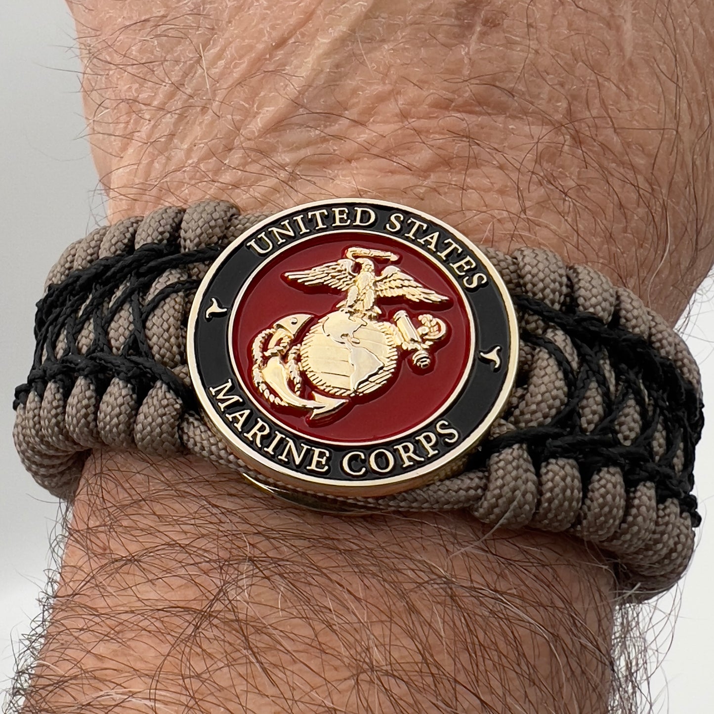 Thick, wide, rigid and comfortable braided United States Marine Corps bracelet featuring a 24K gold plated USMC Eagle Globe and Anchor medallion, a gold Cobra style tactical buckle and woven with tan 550 paracord and black nano and micro cord.