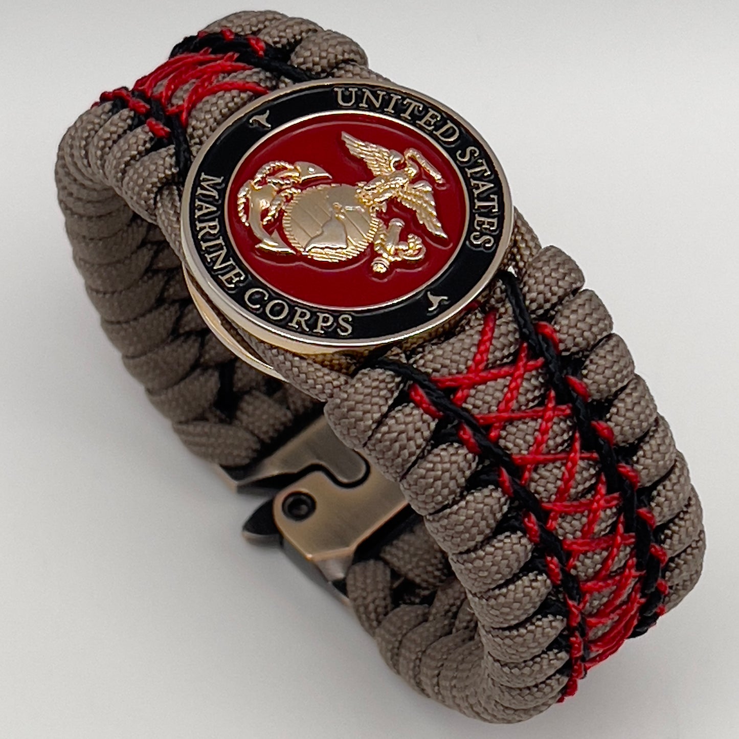 Thick, wide, rigid and comfortable handwoven United States Marine Corps bracelet featuring a 24K gold plated USMC Eagle Globe and Anchor medallion, a gold Cobra style tactical buckle and woven with tna 550 paracord, black micro cord and red nano cord.