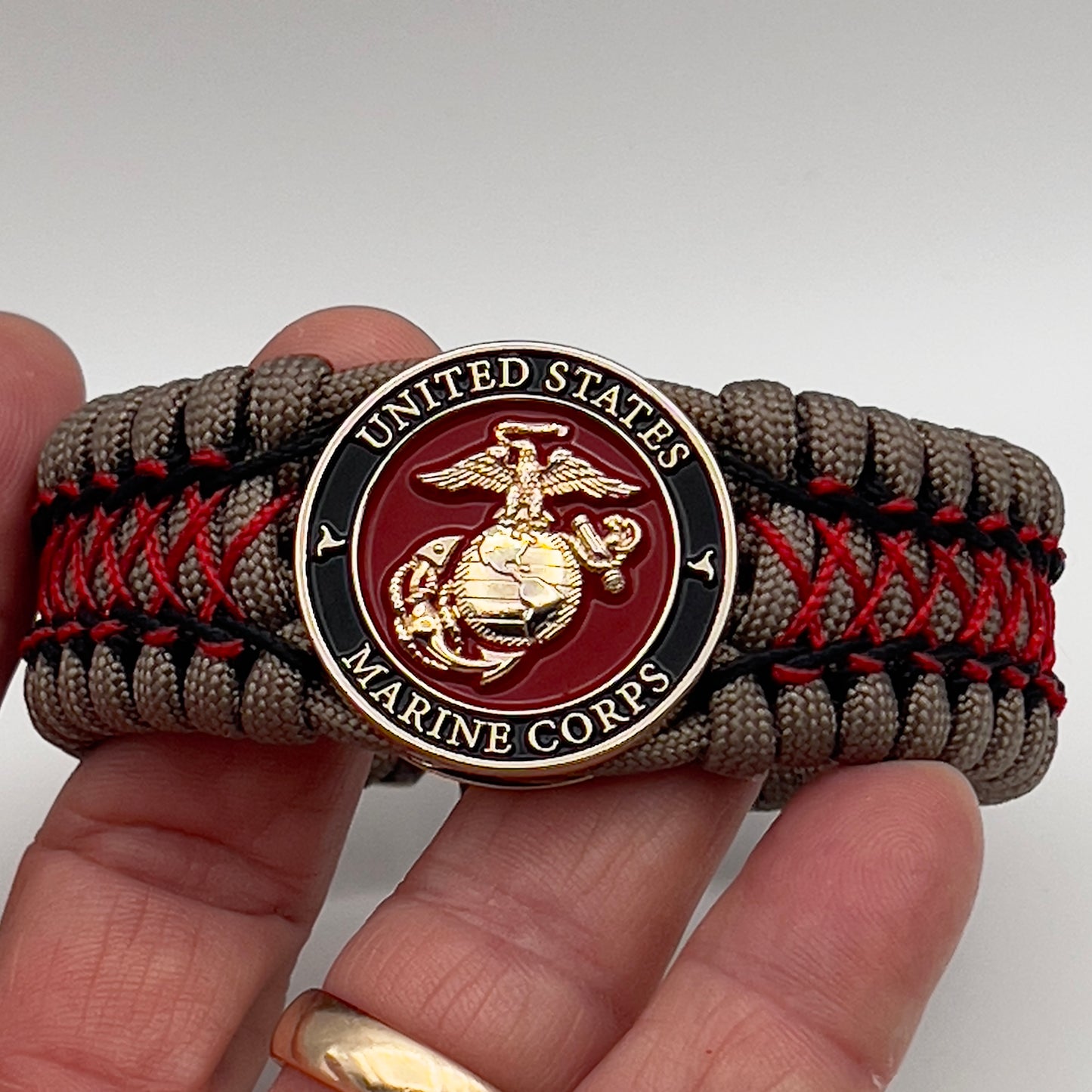 Thick, wide, rigid and comfortable handwoven United States Marine Corps bracelet featuring a 24K gold plated USMC Eagle Globe and Anchor medallion, a gold Cobra style tactical buckle and woven with tna 550 paracord, black micro cord and red nano cord.
