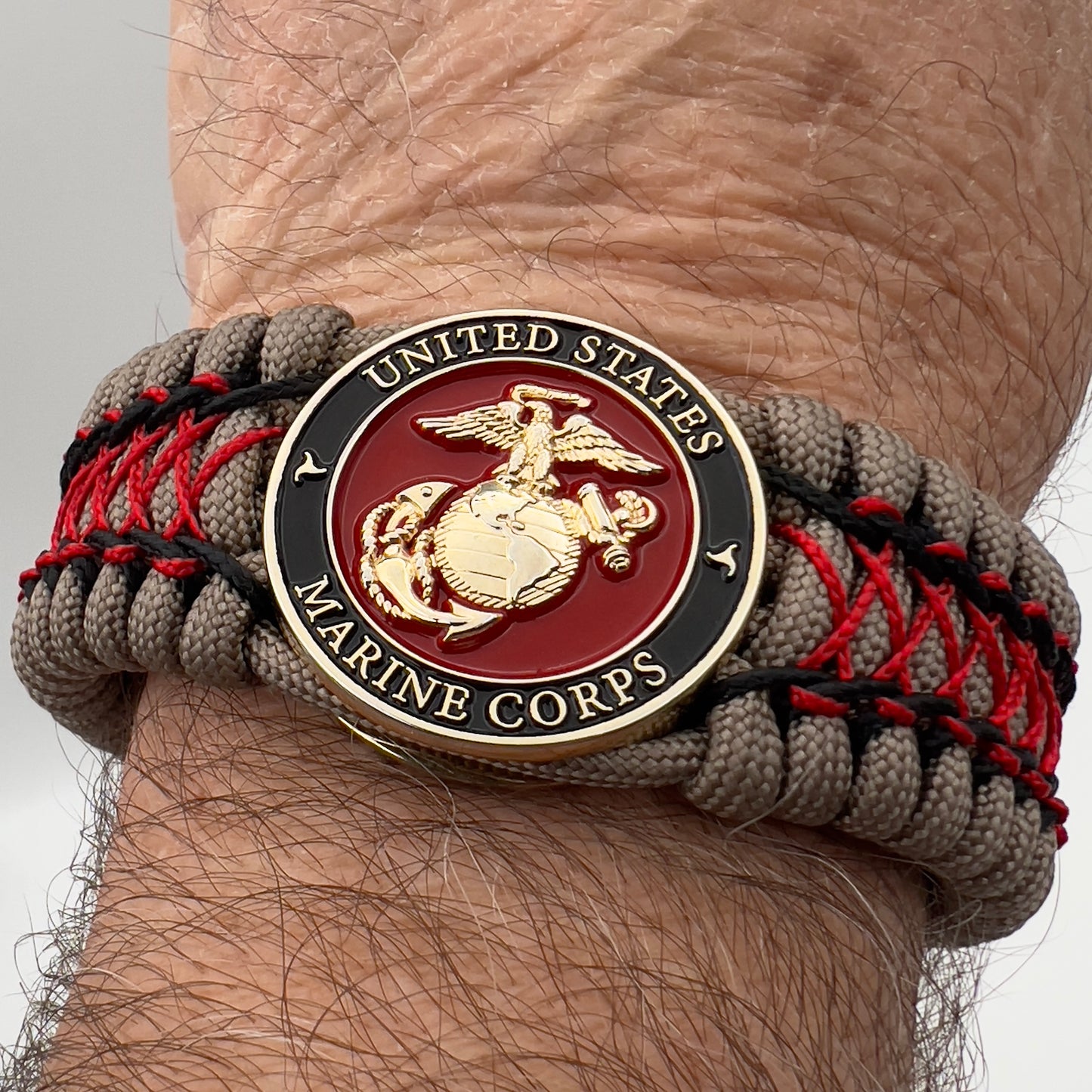 Thick, wide, rigid and comfortable handwoven United States Marine Corps bracelet featuring a 24K gold plated USMC Eagle Globe and Anchor medallion, a gold Cobra style tactical buckle and woven with tna 550 paracord, black micro cord and red nano cord.