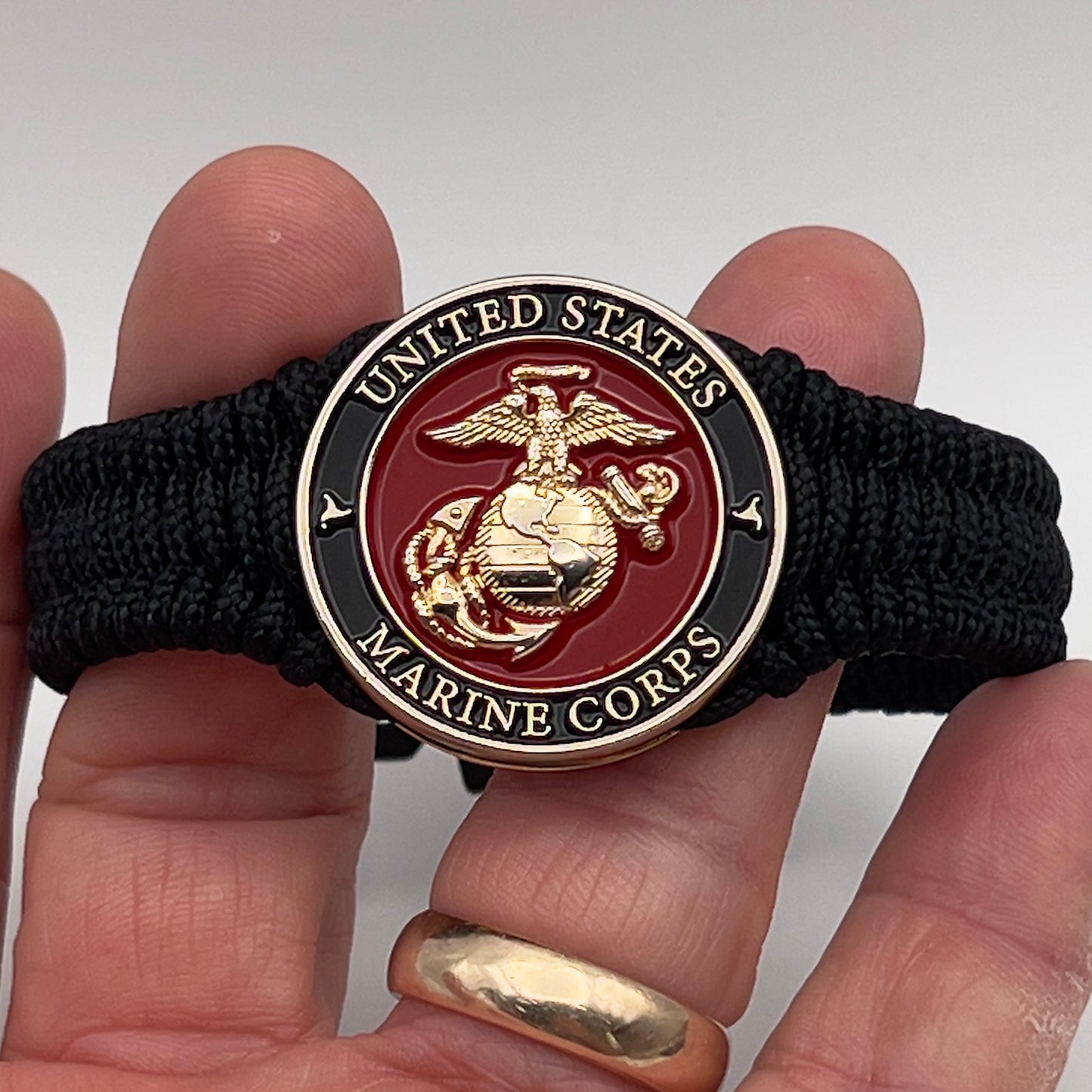 Thick, narrow, flexible and comfortable braided United States Marine Corps bracelet featuring a 24K gold plated USMC officer Eagle Globe and Anchor medallion, a black Cobra style tactical buckle and woven with black Type-1 paracord.