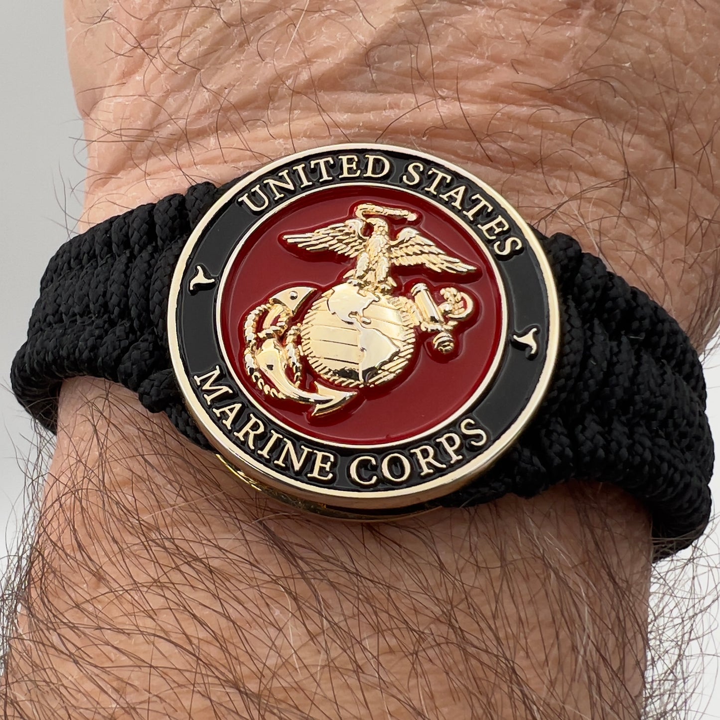 Thick, narrow, flexible and comfortable braided United States Marine Corps bracelet featuring a 24K gold plated USMC officer Eagle Globe and Anchor medallion, a black Cobra style tactical buckle and woven with black Type-1 paracord.