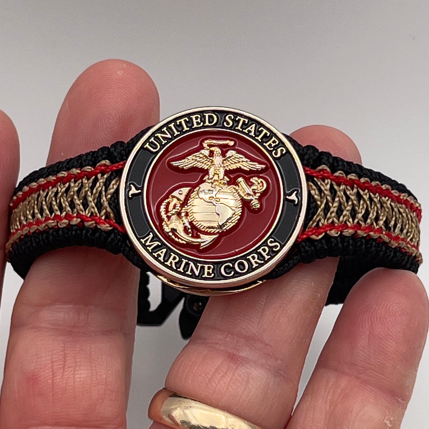 Thin, narrow, flexible and comfortable braided United States Marine Corps bracelet featuring a 24K gold plated USMC Eagle Globe and Anchor medallion, a black Cobra style tactical buckle and woven with black Type-1 paracord and Imperial Red and Gold nano cord.