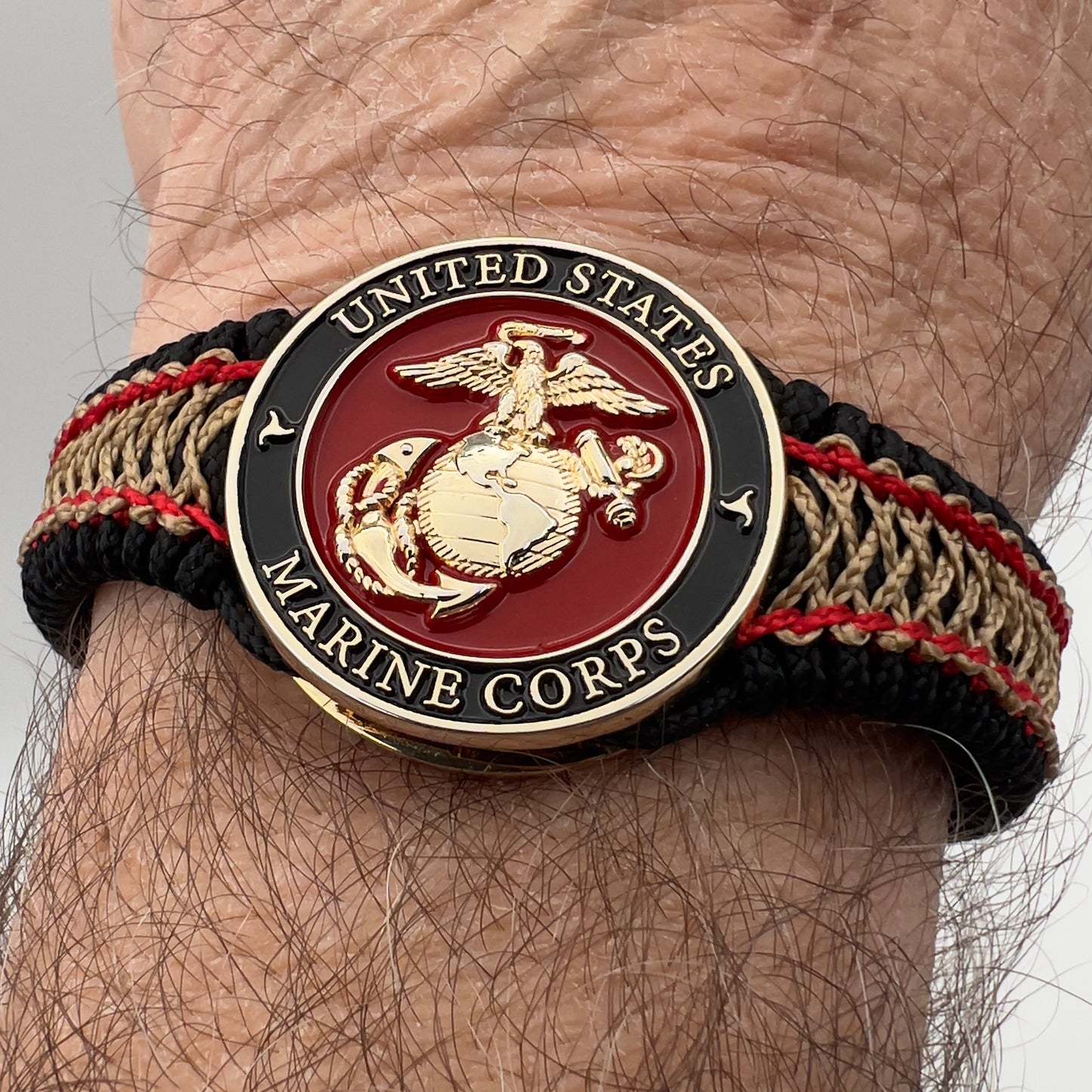 Thin, narrow, flexible and comfortable braided United States Marine Corps bracelet featuring a 24K gold plated USMC Eagle Globe and Anchor medallion, a black Cobra style tactical buckle and woven with black Type-1 paracord and Imperial Red and Gold nano cord.