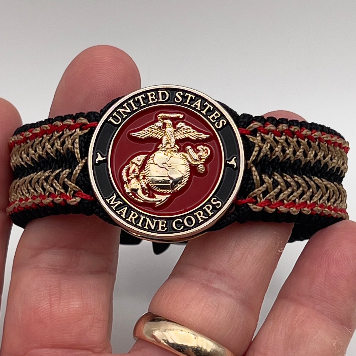 Thin, narrow, flexible and comfortable braided United States Marine Corps bracelet featuring a 24K gold plated USMC Eagle Globe and Anchor medallion, a black Cobra style tactical buckle and woven with black Type-1 paracord and Imperial Red and Gold nano cord.