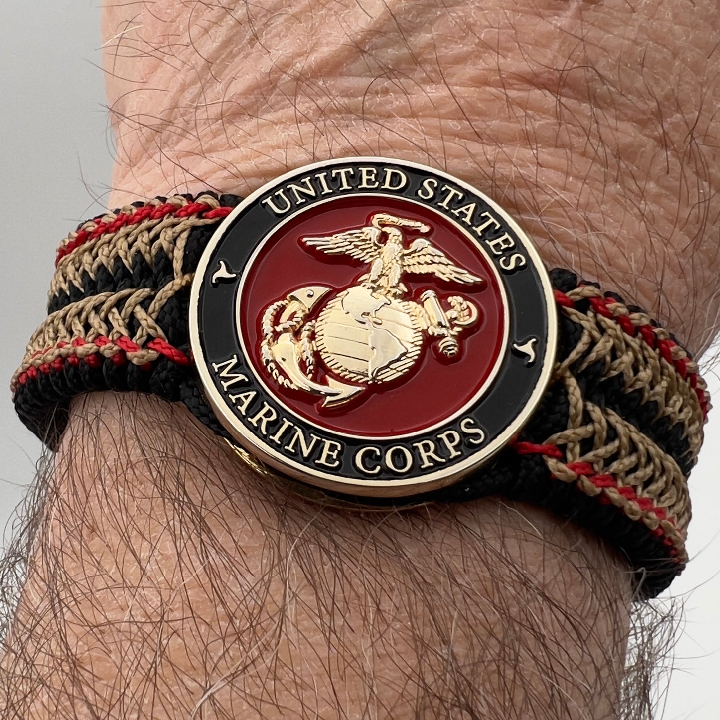 Thin, narrow, flexible and comfortable braided United States Marine Corps bracelet featuring a 24K gold plated USMC Eagle Globe and Anchor medallion, a black Cobra style tactical buckle and woven with black Type-1 paracord and Imperial Red and Gold nano cord.