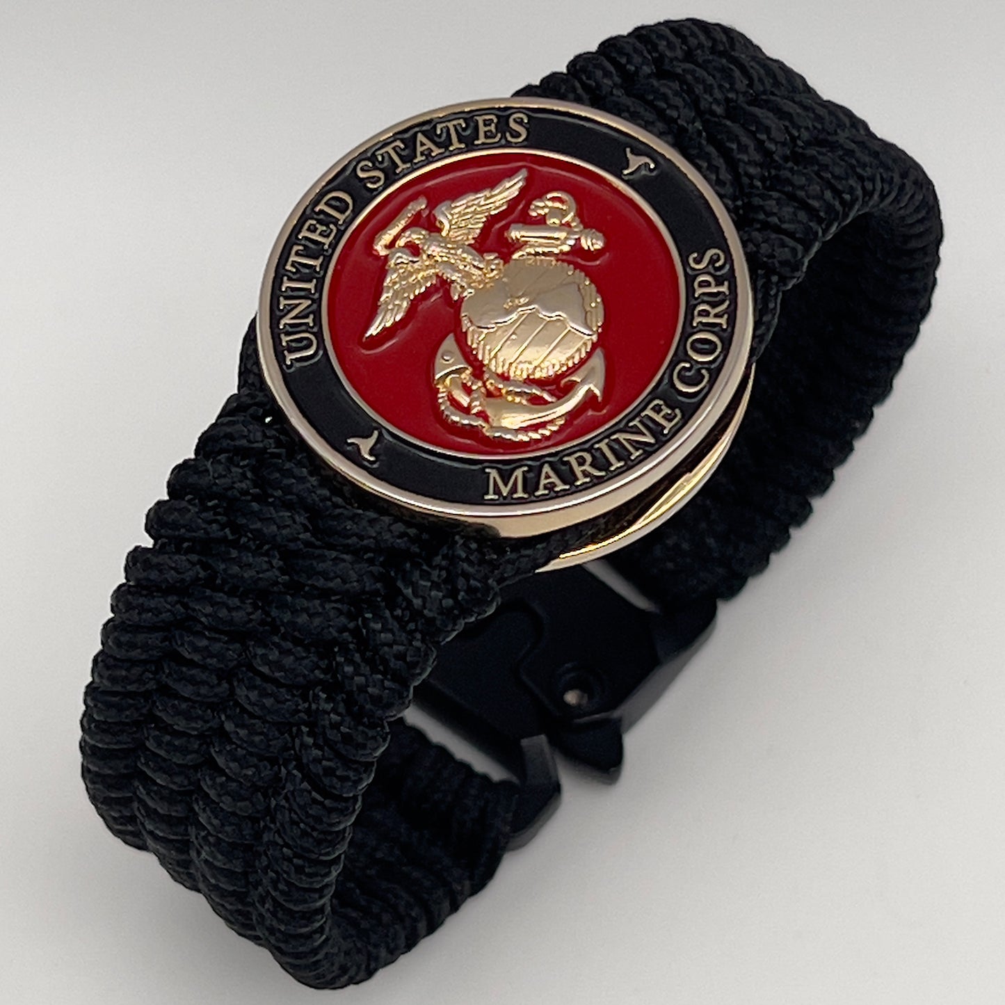 Thin, medium width, flexible and comfortable braided United States Marine Corps bracelet featuring a 24K gold plated USMC officer Eagle Globe and Anchor medallion, a black Cobra style tactical buckle and woven with black Type-1 paracord.