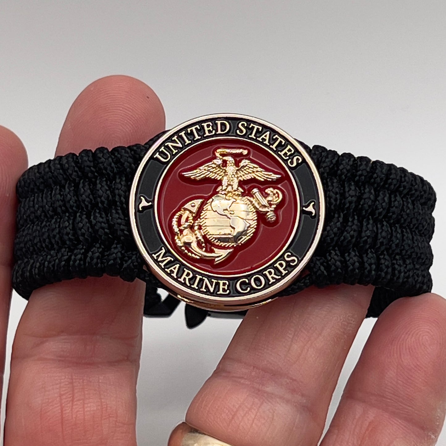 Thin, medium width, flexible and comfortable braided United States Marine Corps bracelet featuring a 24K gold plated USMC officer Eagle Globe and Anchor medallion, a black Cobra style tactical buckle and woven with black Type-1 paracord.