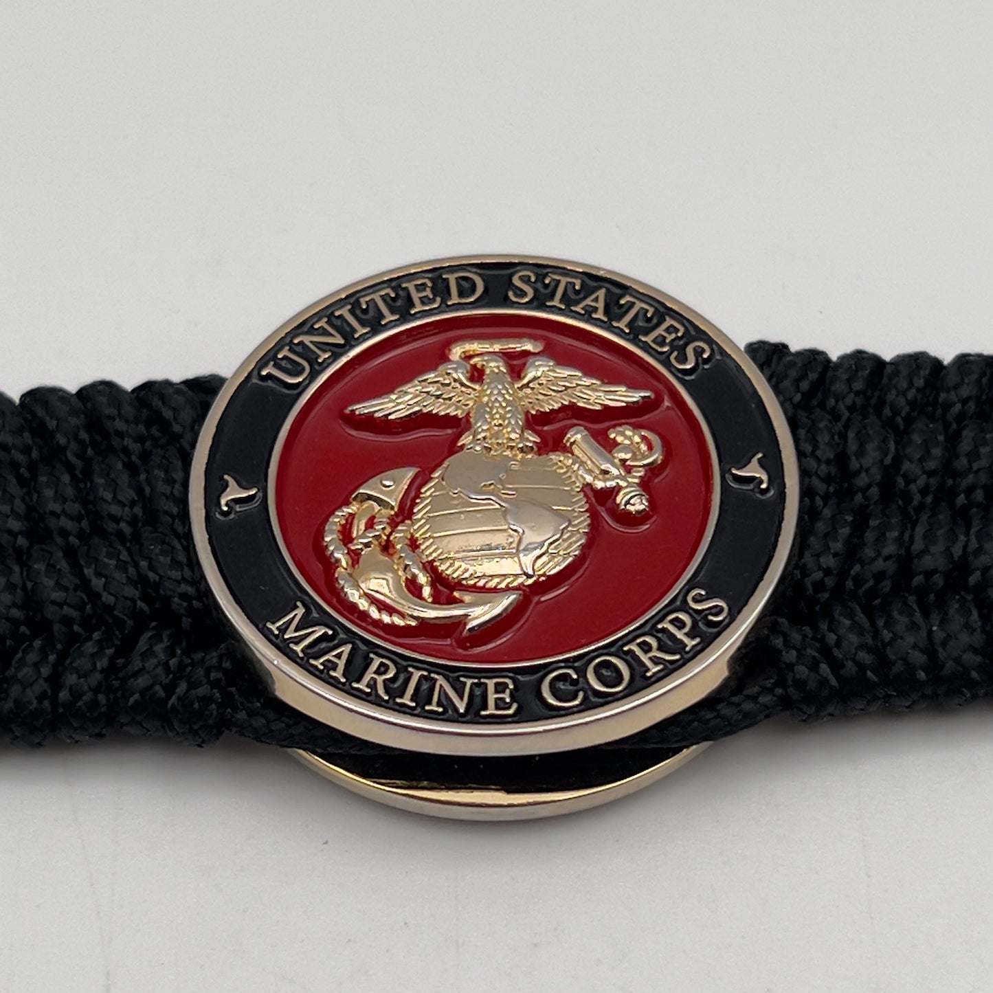 Thin, medium width, flexible and comfortable braided United States Marine Corps bracelet featuring a 24K gold plated USMC officer Eagle Globe and Anchor medallion, a black Cobra style tactical buckle and woven with black Type-1 paracord.
