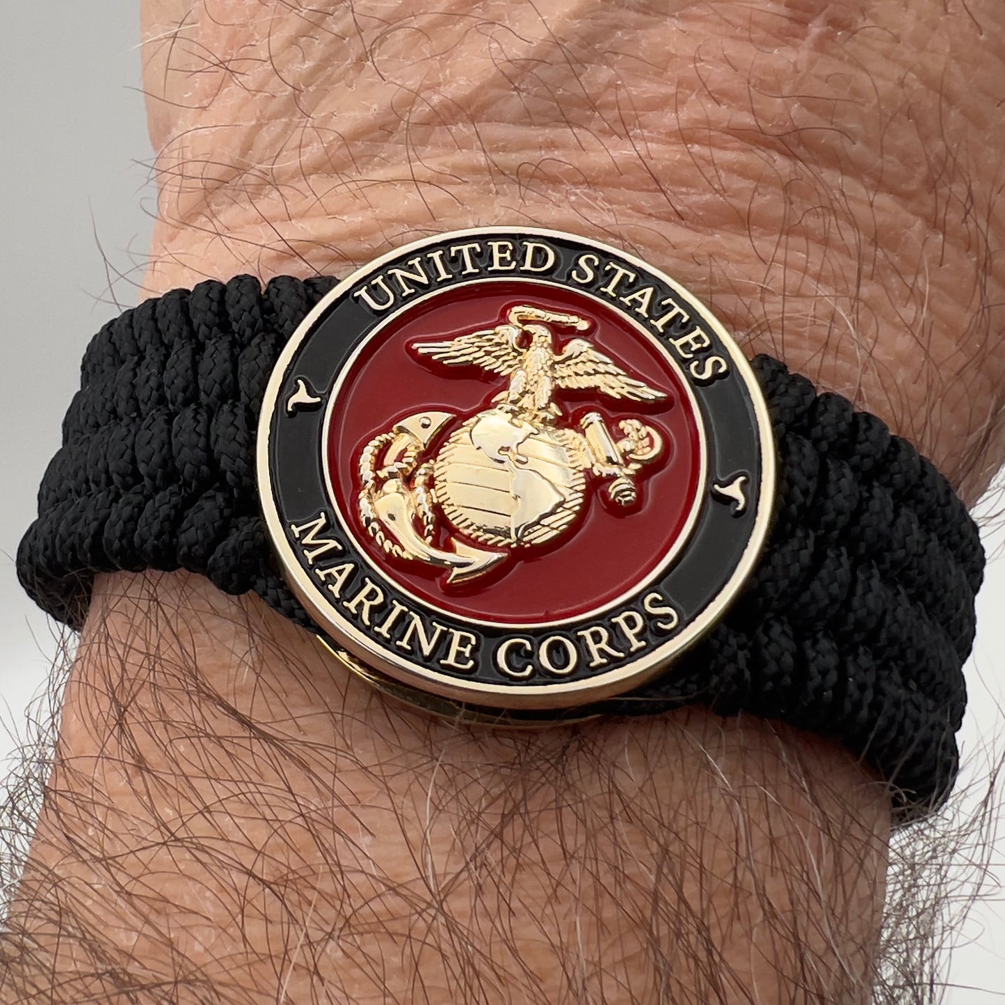 Thin, medium width, flexible and comfortable braided United States Marine Corps bracelet featuring a 24K gold plated USMC officer Eagle Globe and Anchor medallion, a black Cobra style tactical buckle and woven with black Type-1 paracord.