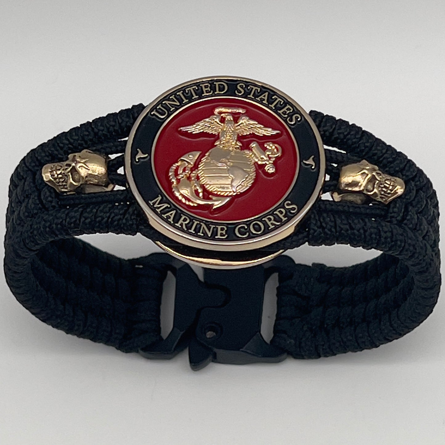 Thin, medium width, flexible and comfortable braided United States Marine Corps bracelet featuring a 24K gold plated USMC officer Eagle Globe and Anchor medallion, two gold plated skulls, a black Cobra style tactical buckle and woven with black Type-1 paracord.