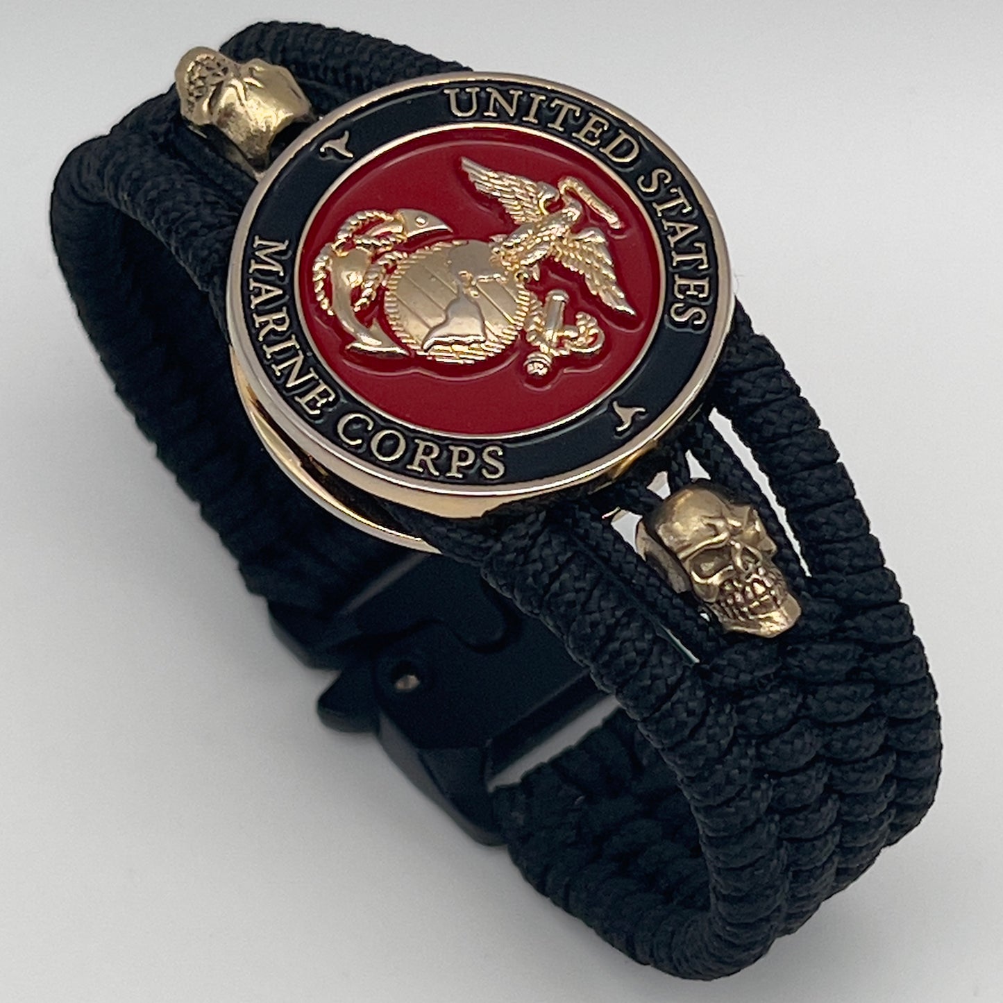 Thin, medium width, flexible and comfortable braided United States Marine Corps bracelet featuring a 24K gold plated USMC officer Eagle Globe and Anchor medallion, two gold plated skulls, a black Cobra style tactical buckle and woven with black Type-1 paracord.
