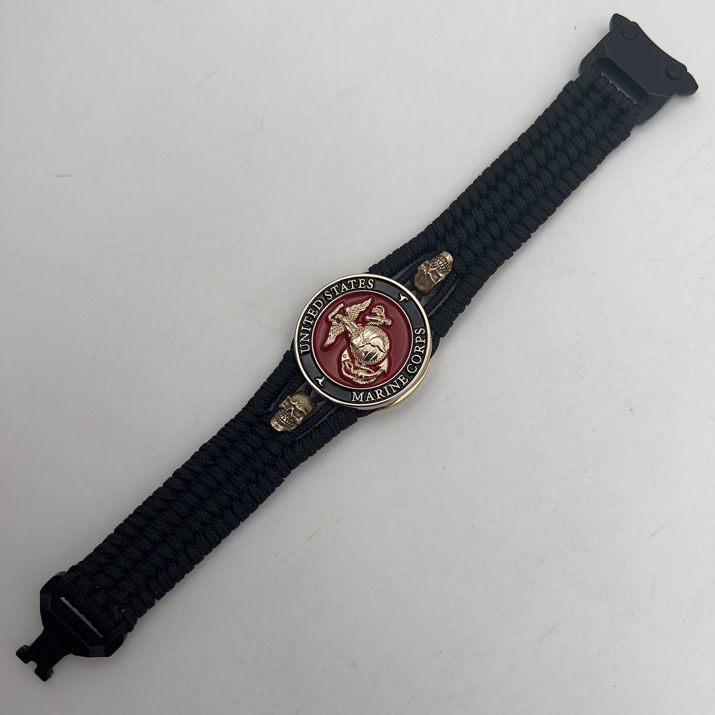 Thin, medium width, flexible and comfortable braided United States Marine Corps bracelet featuring a 24K gold plated USMC officer Eagle Globe and Anchor medallion, two gold plated skulls, a black Cobra style tactical buckle and woven with black Type-1 paracord.