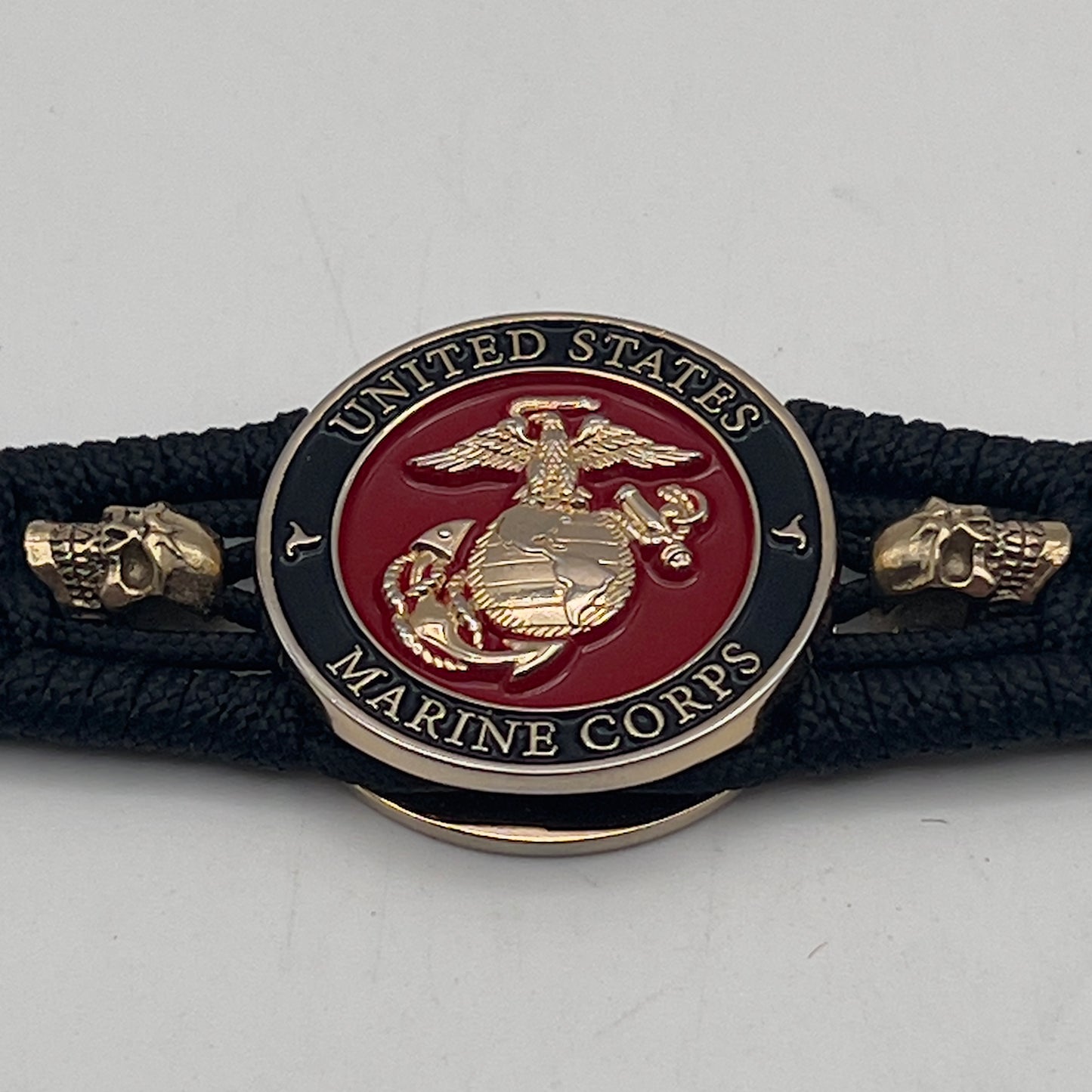 Thin, medium width, flexible and comfortable braided United States Marine Corps bracelet featuring a 24K gold plated USMC officer Eagle Globe and Anchor medallion, two gold plated skulls, a black Cobra style tactical buckle and woven with black Type-1 paracord.