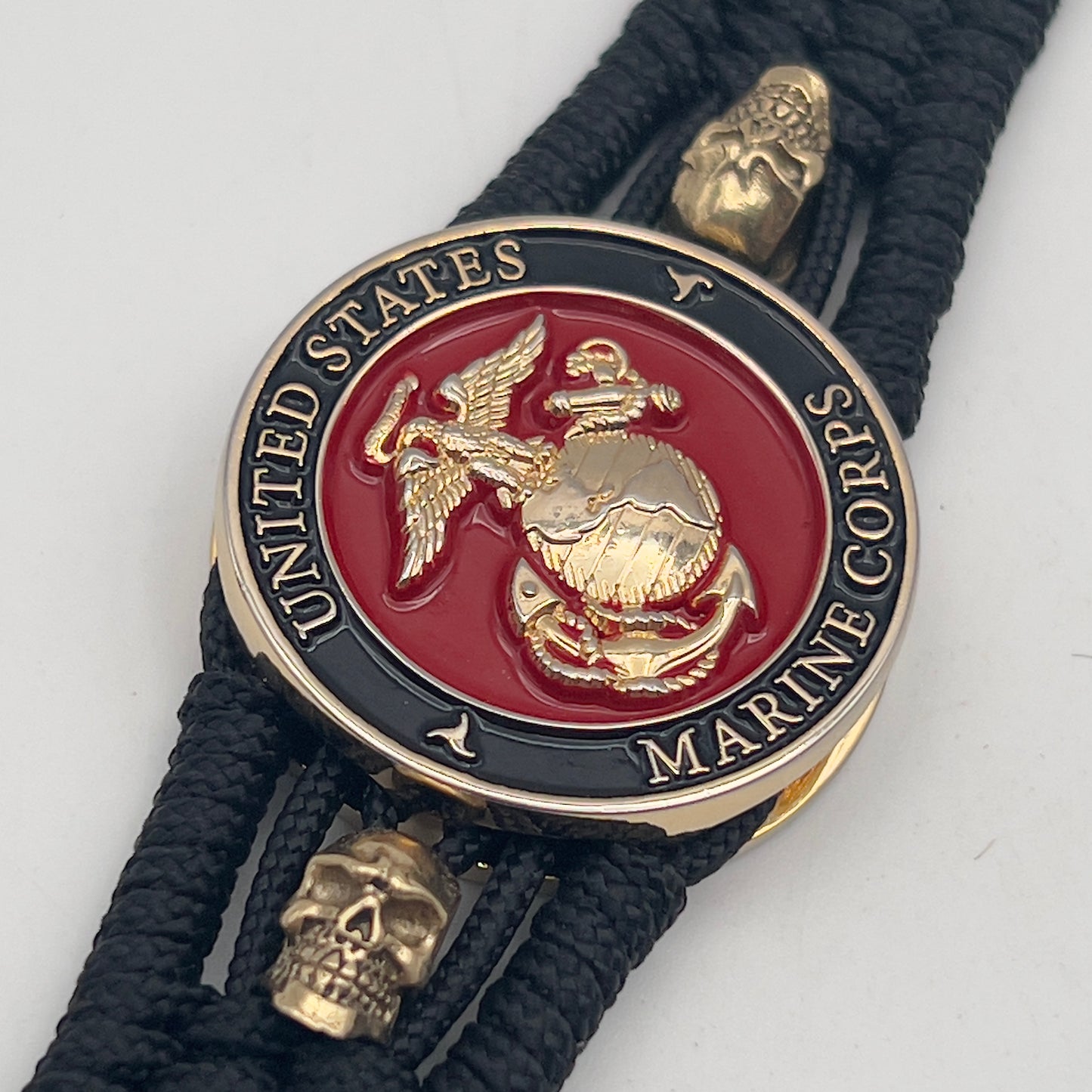 Thin, medium width, flexible and comfortable braided United States Marine Corps bracelet featuring a 24K gold plated USMC officer Eagle Globe and Anchor medallion, two gold plated skulls, a black Cobra style tactical buckle and woven with black Type-1 paracord.
