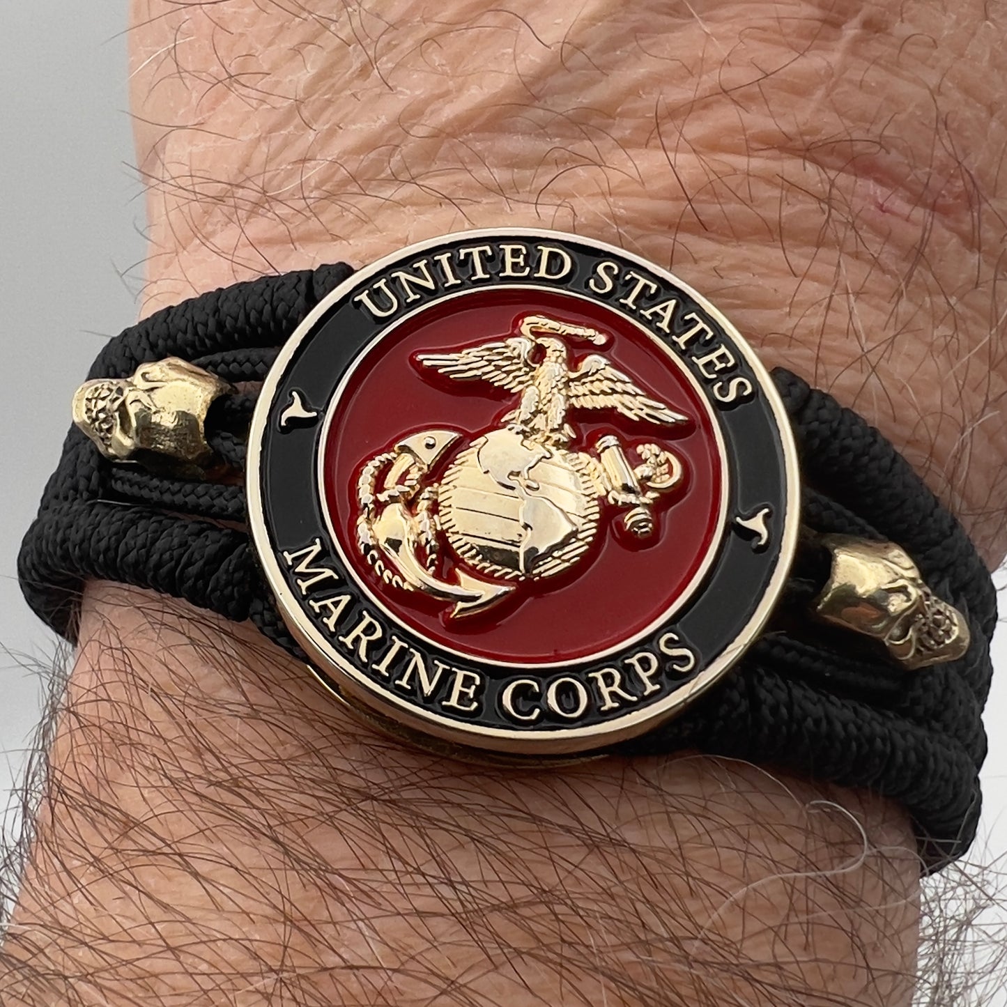 Thin, medium width, flexible and comfortable braided United States Marine Corps bracelet featuring a 24K gold plated USMC officer Eagle Globe and Anchor medallion, two gold plated skulls, a black Cobra style tactical buckle and woven with black Type-1 paracord.