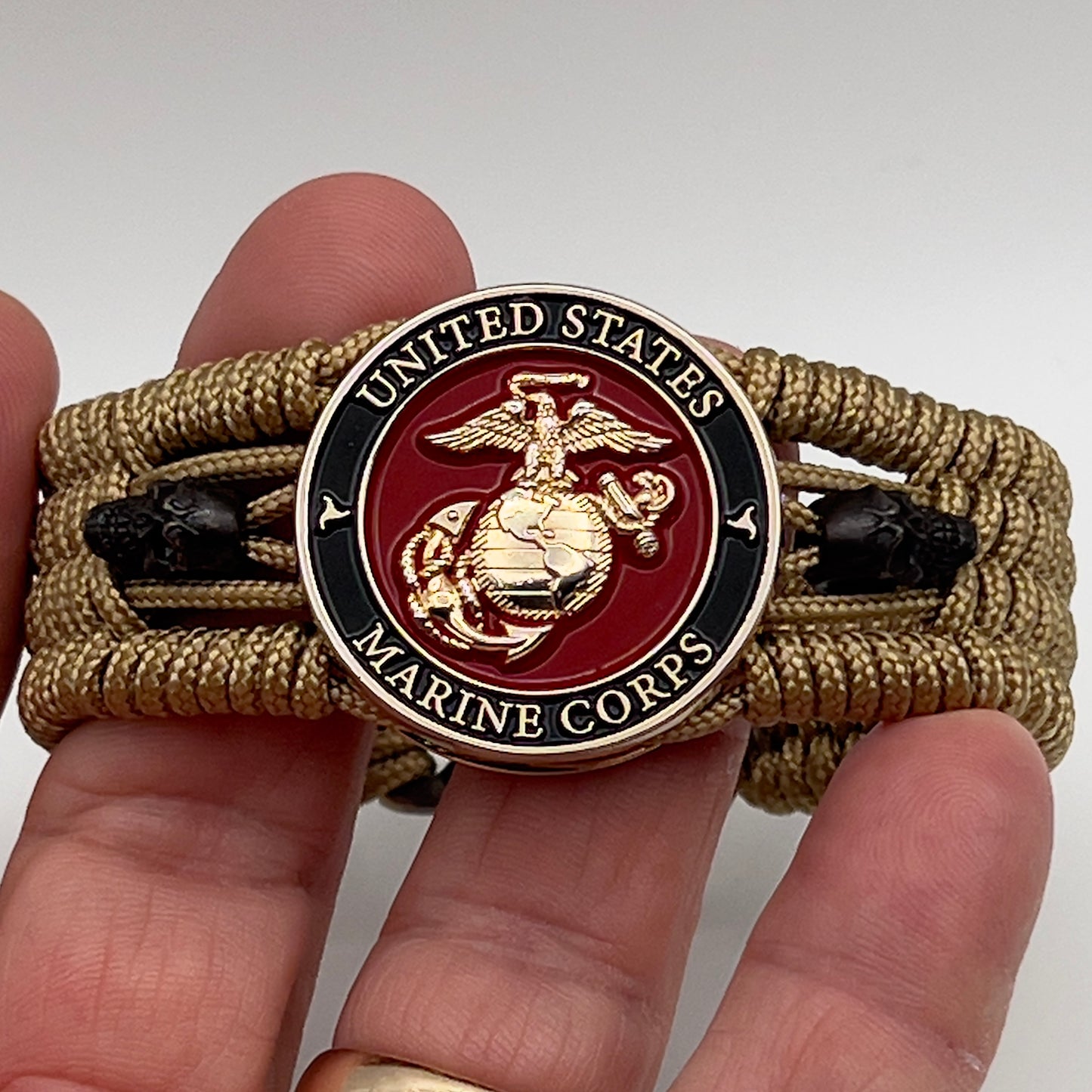 Thin, medium width, flexible and comfortable braided United States Marine Corps bracelet featuring a 24K gold plated USMC officer Eagle Globe and Anchor medallion, two black micro skulls, a gold Cobra style tactical buckle and woven with gold Type-1 paracord.