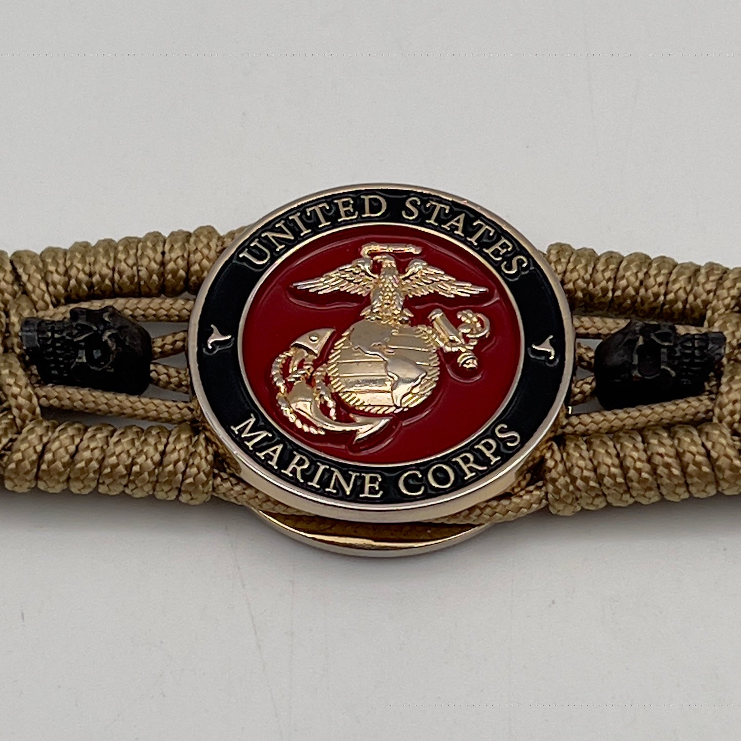 Thin, medium width, flexible and comfortable braided United States Marine Corps bracelet featuring a 24K gold plated USMC officer Eagle Globe and Anchor medallion, two black micro skulls, a gold Cobra style tactical buckle and woven with gold Type-1 paracord.