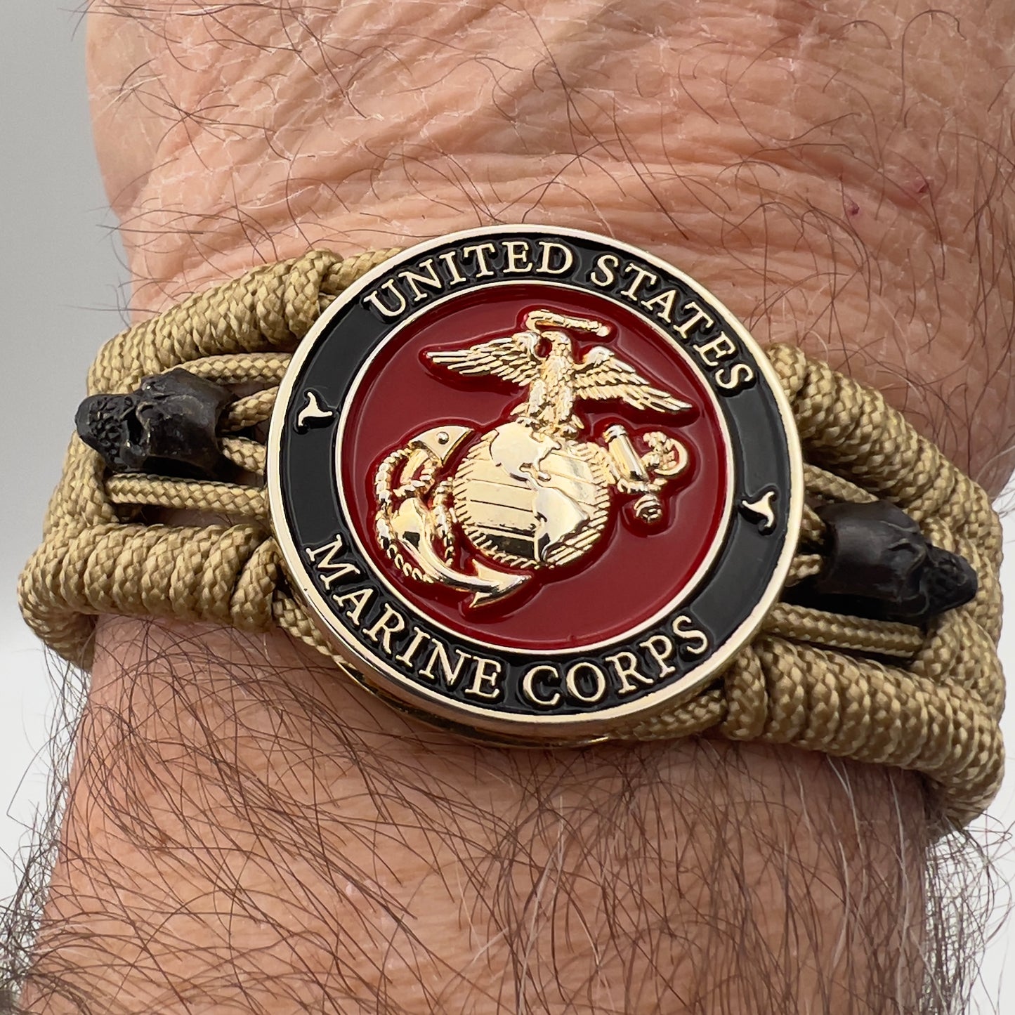 Thin, medium width, flexible and comfortable braided United States Marine Corps bracelet featuring a 24K gold plated USMC officer Eagle Globe and Anchor medallion, two black micro skulls, a gold Cobra style tactical buckle and woven with gold Type-1 paracord.