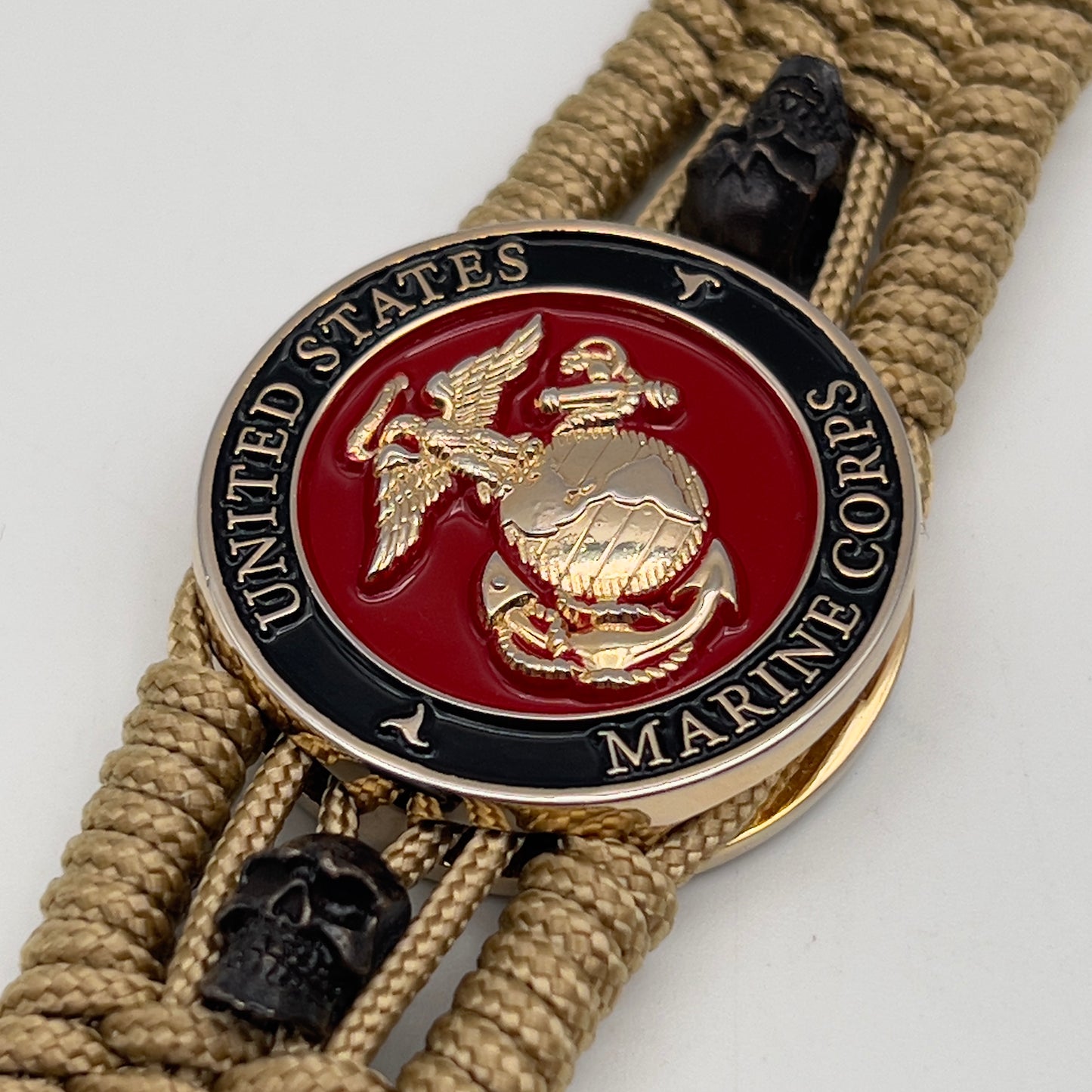 Thin, medium width, flexible and comfortable braided United States Marine Corps bracelet featuring a 24K gold plated USMC officer Eagle Globe and Anchor medallion, two black micro skulls, a gold Cobra style tactical buckle and woven with gold Type-1 paracord.